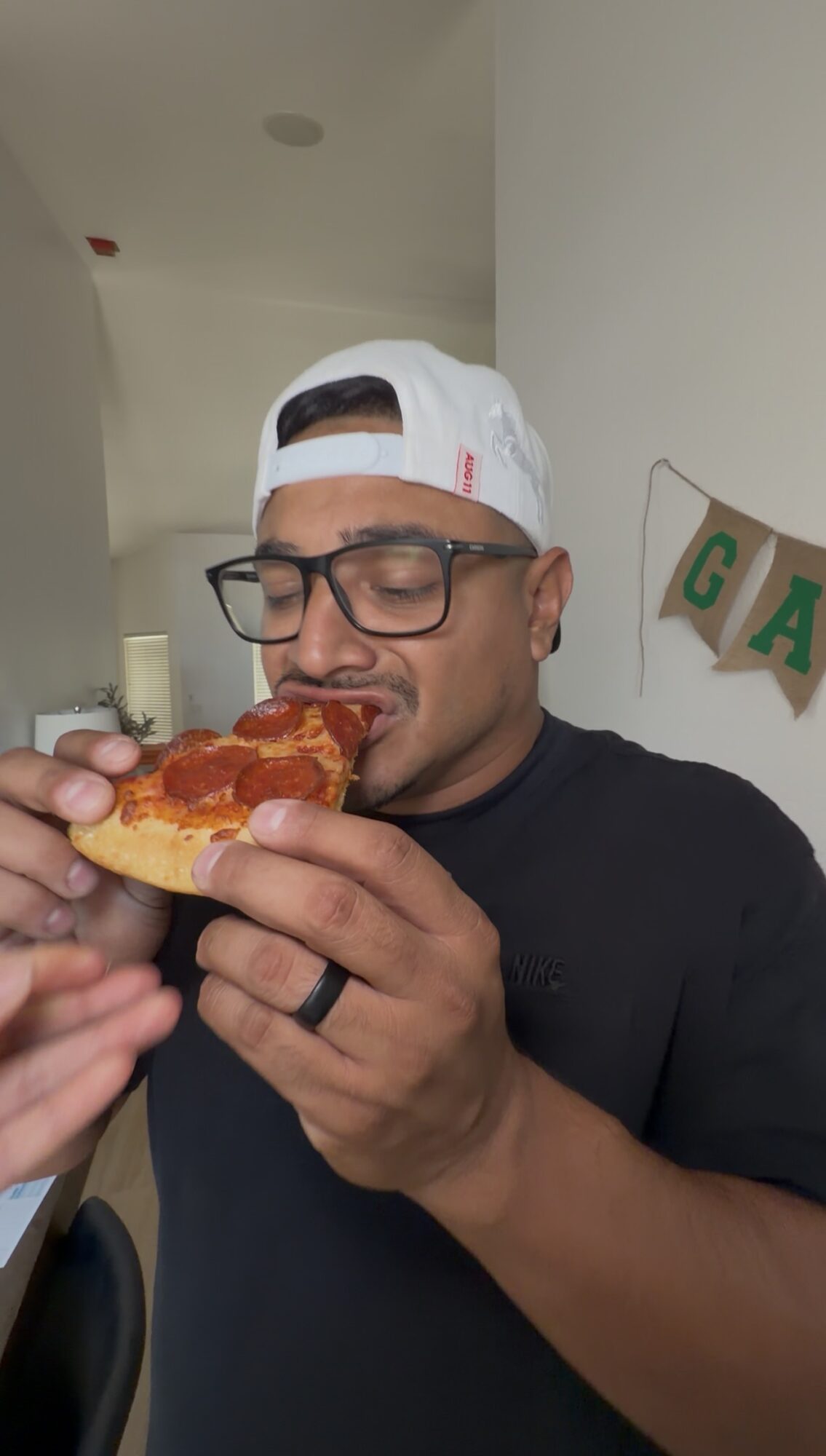 Person wearing glasses and a white cap eating a slice of pizza, with a decorated background.