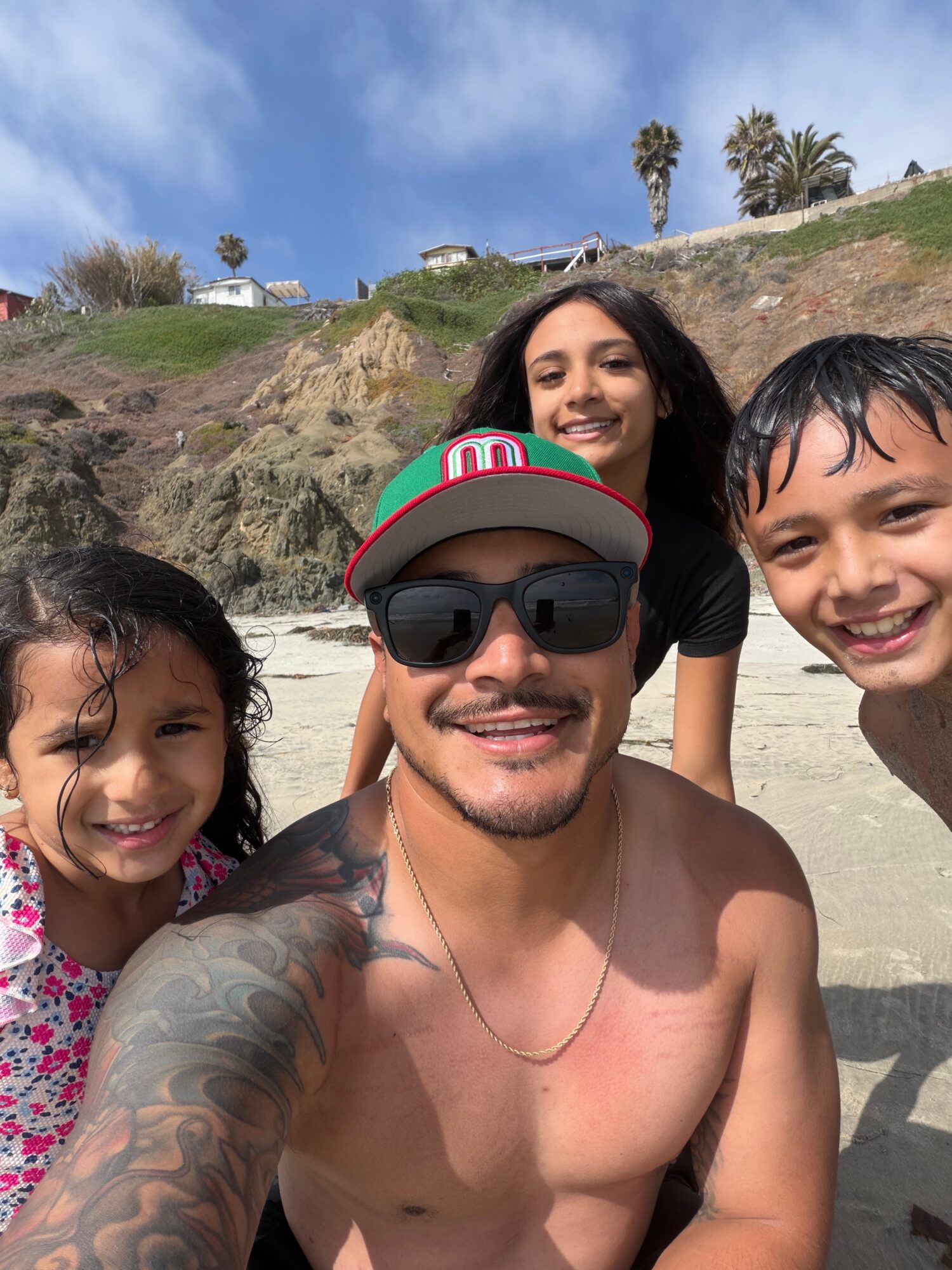 Group of four people smiling on a beach with cliffs and palm trees in the background.