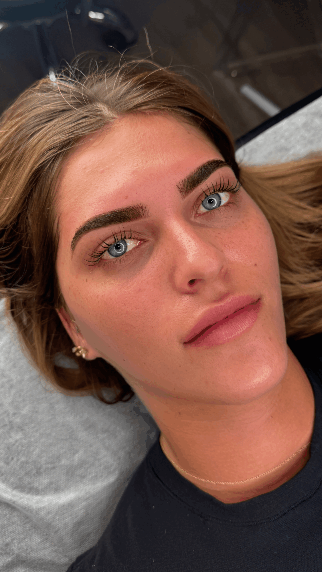 Close-up of a woman with blue eyes, brown hair, and makeup, lying down and looking at the camera.
