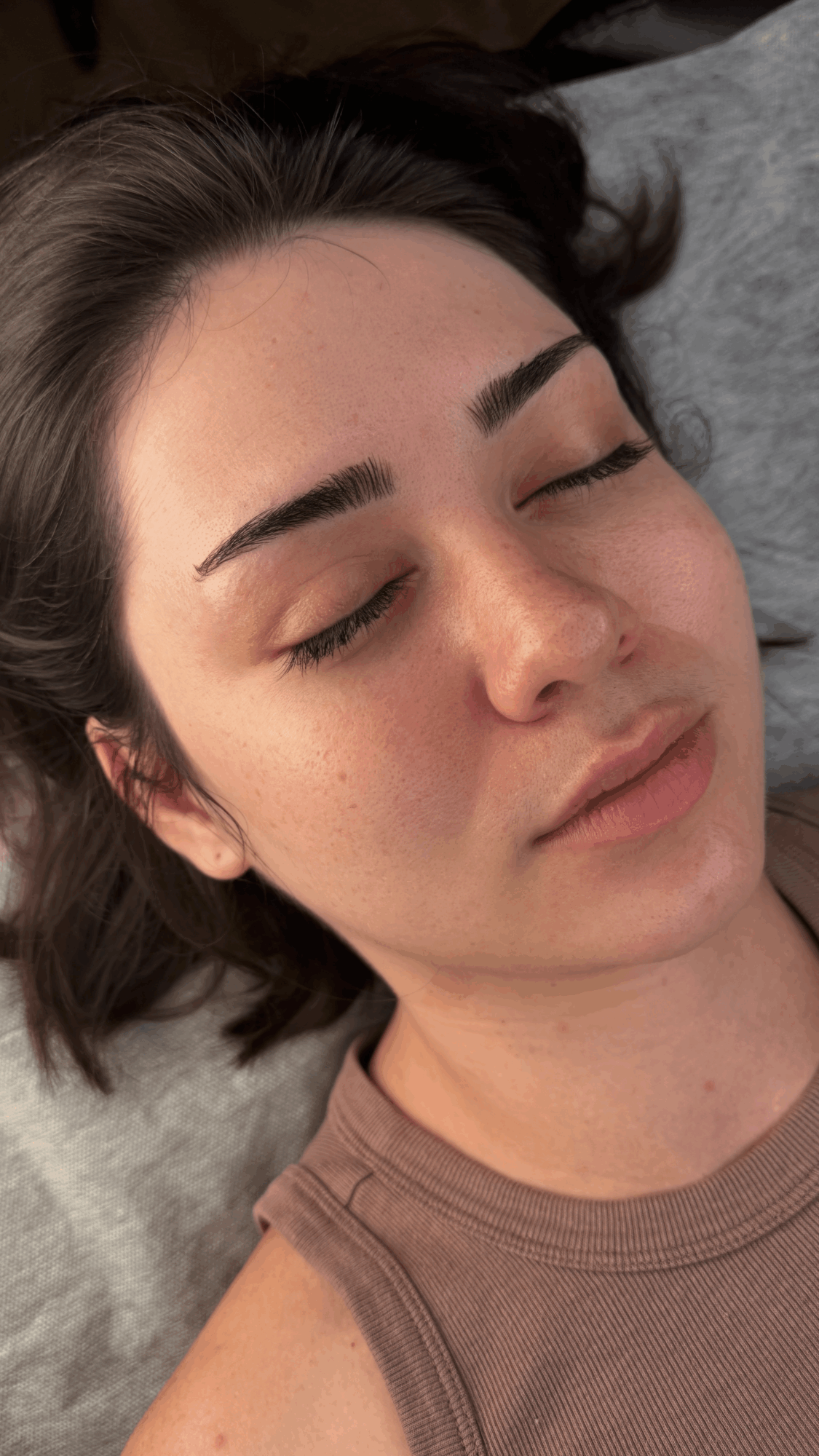 Close-up of a young woman with closed eyes, dark eyebrows, and long hair lying on a pillow.