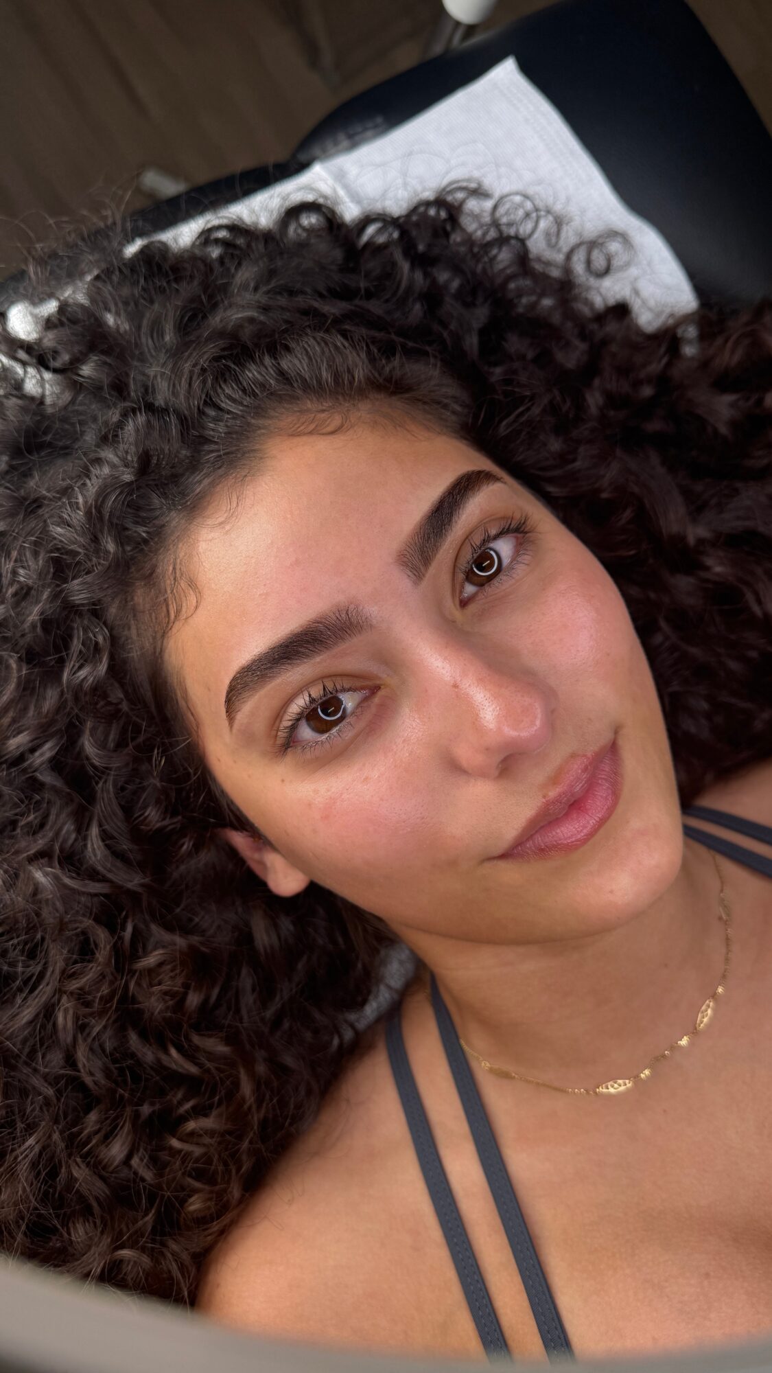 Young woman with curly hair lying down, looking at the camera, wearing a striped top and a necklace.