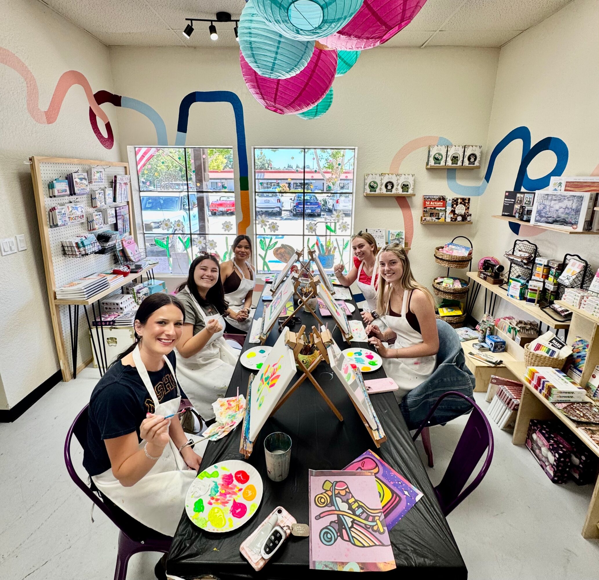 Group of children painting at a table in an art classroom with colorful decorations and supplies.