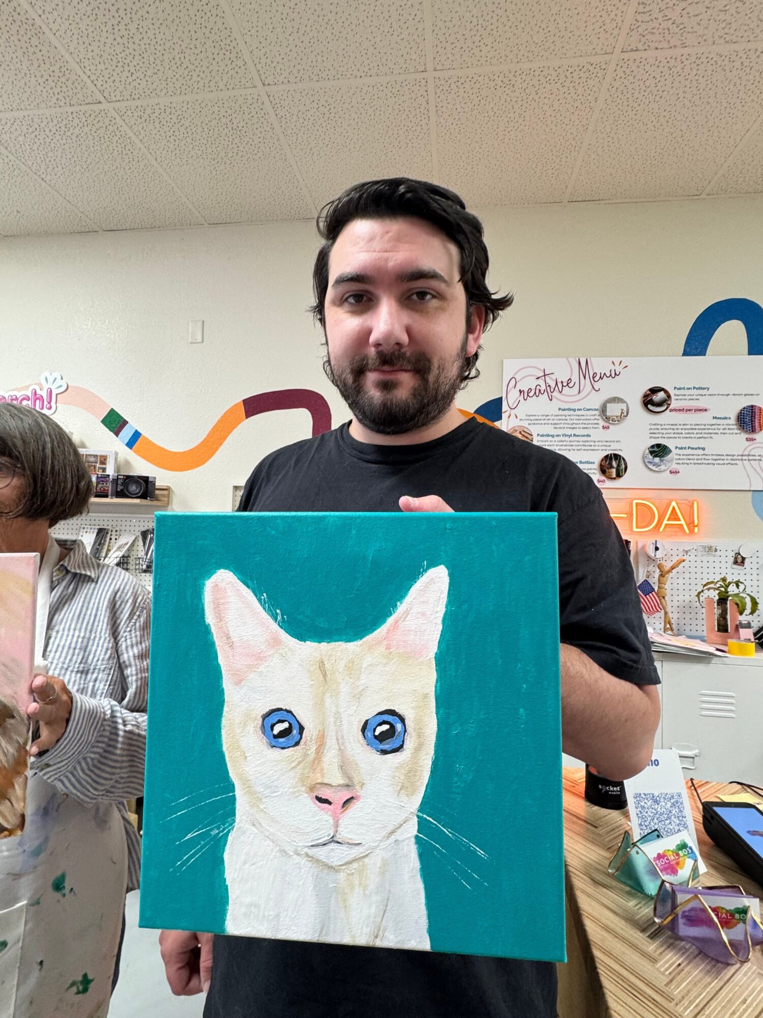 Person holding a painting of a white cat with blue eyes against a teal background.