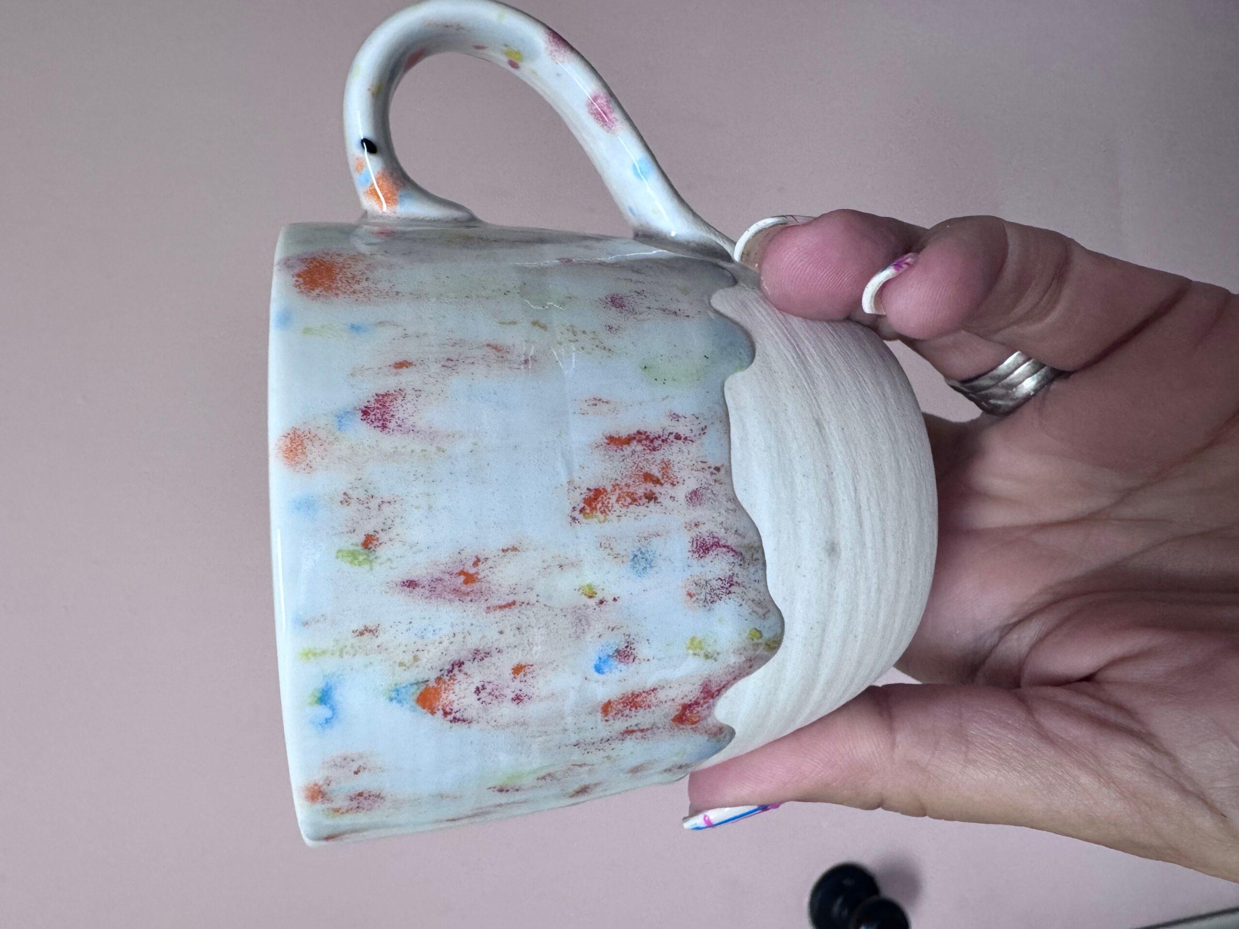 Person holding a colorful, weathered ceramic mug with a handle, against a plain background.