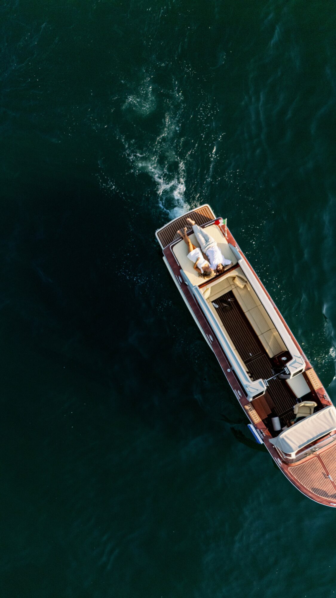 A boat moving through dark green water, creating a wake behind it, viewed from above.