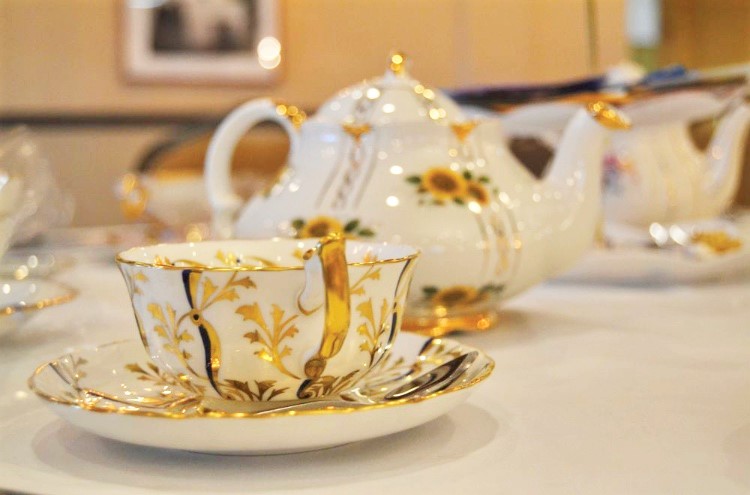 Elegant teapot and cup with gold and floral designs on a table, with other teapots in the background.