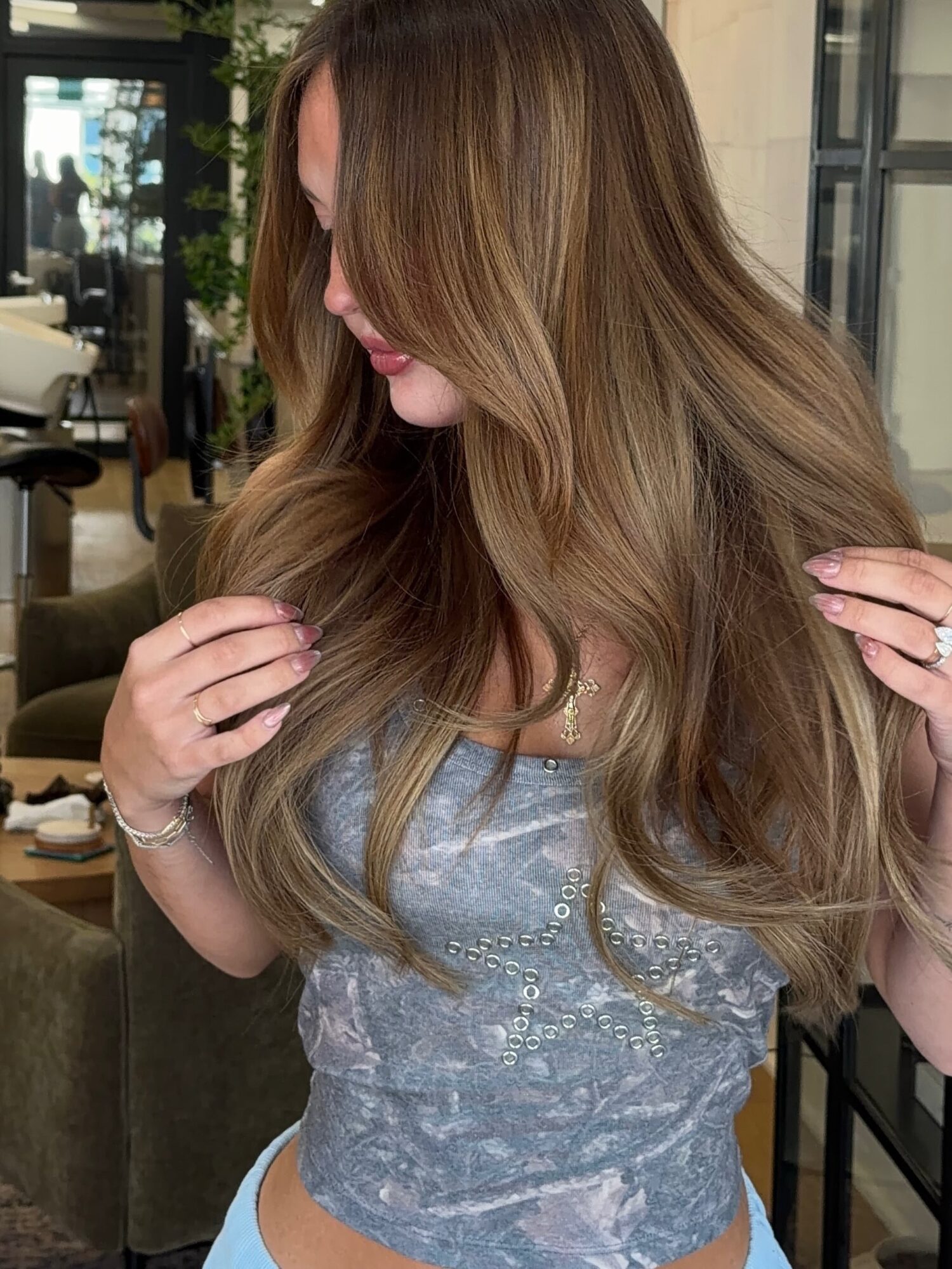 Woman with long, wavy, light brown hair looking down, wearing a gray top, in an indoor setting.