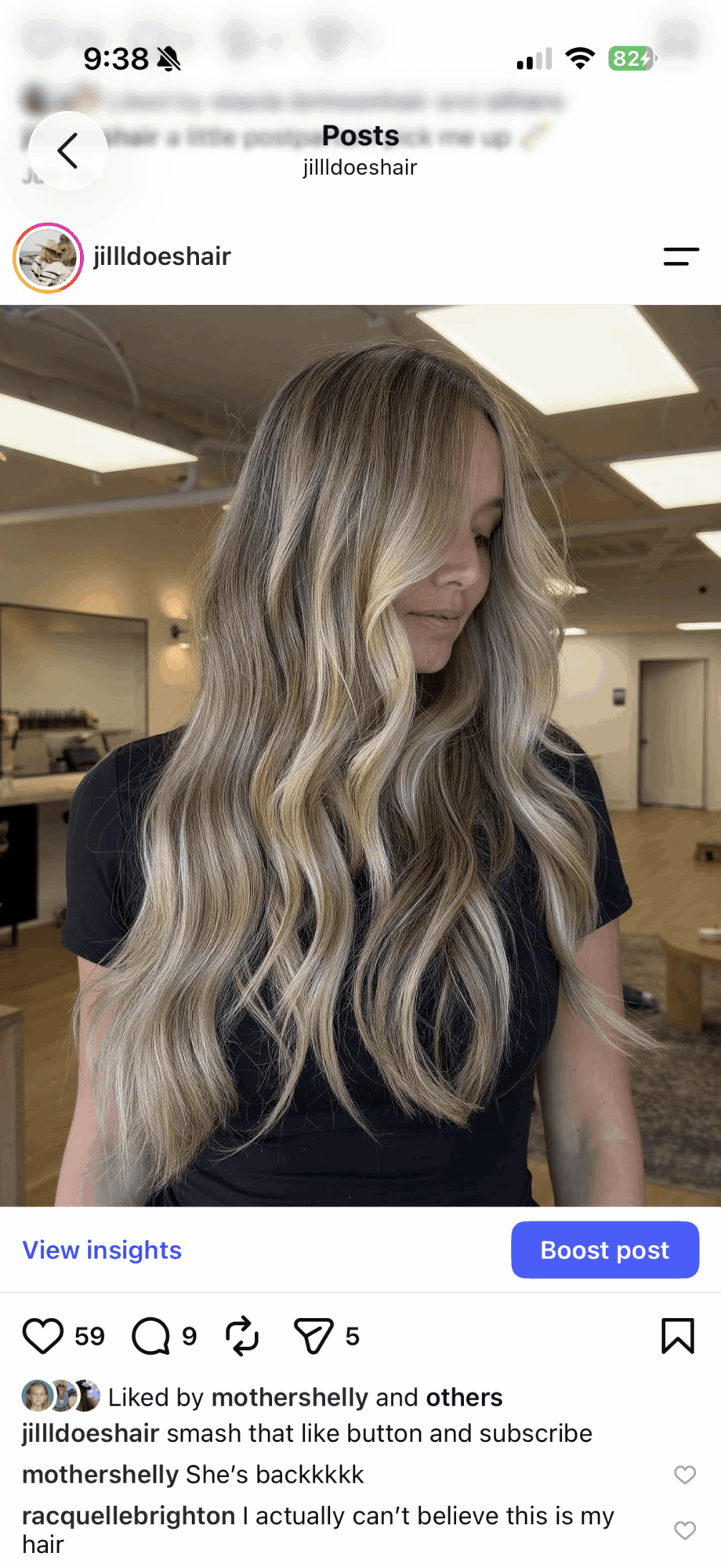 Woman with long wavy blonde hair in a black top, indoors, facing right, smiling slightly.