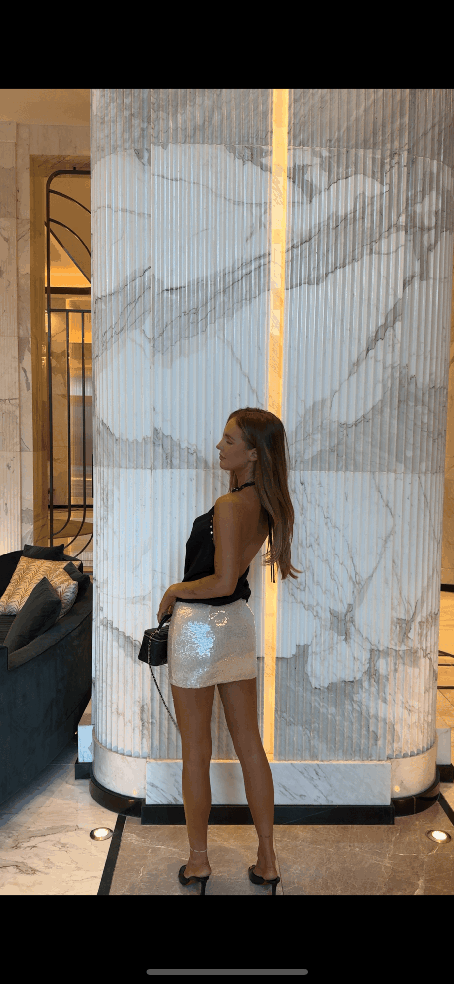 Woman standing in front of a large marble wall, holding a camera, with a sofa nearby.