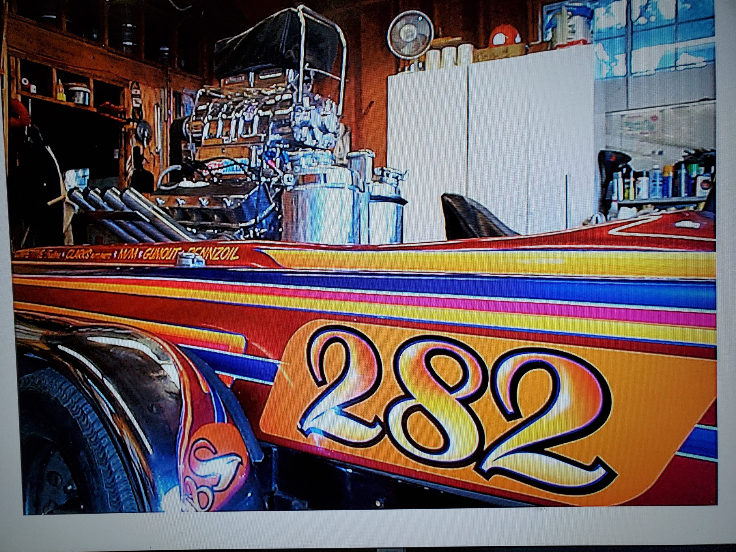A colorful boat with the number 282 on its side, inside a workshop with tools and equipment visible in the background.