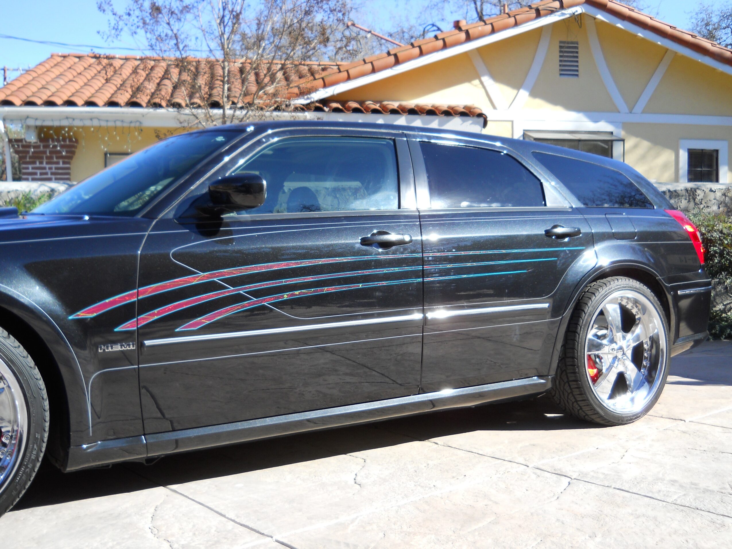 Black station wagon with colorful stripe decals parked in front of a house with a yellow and white exterior.