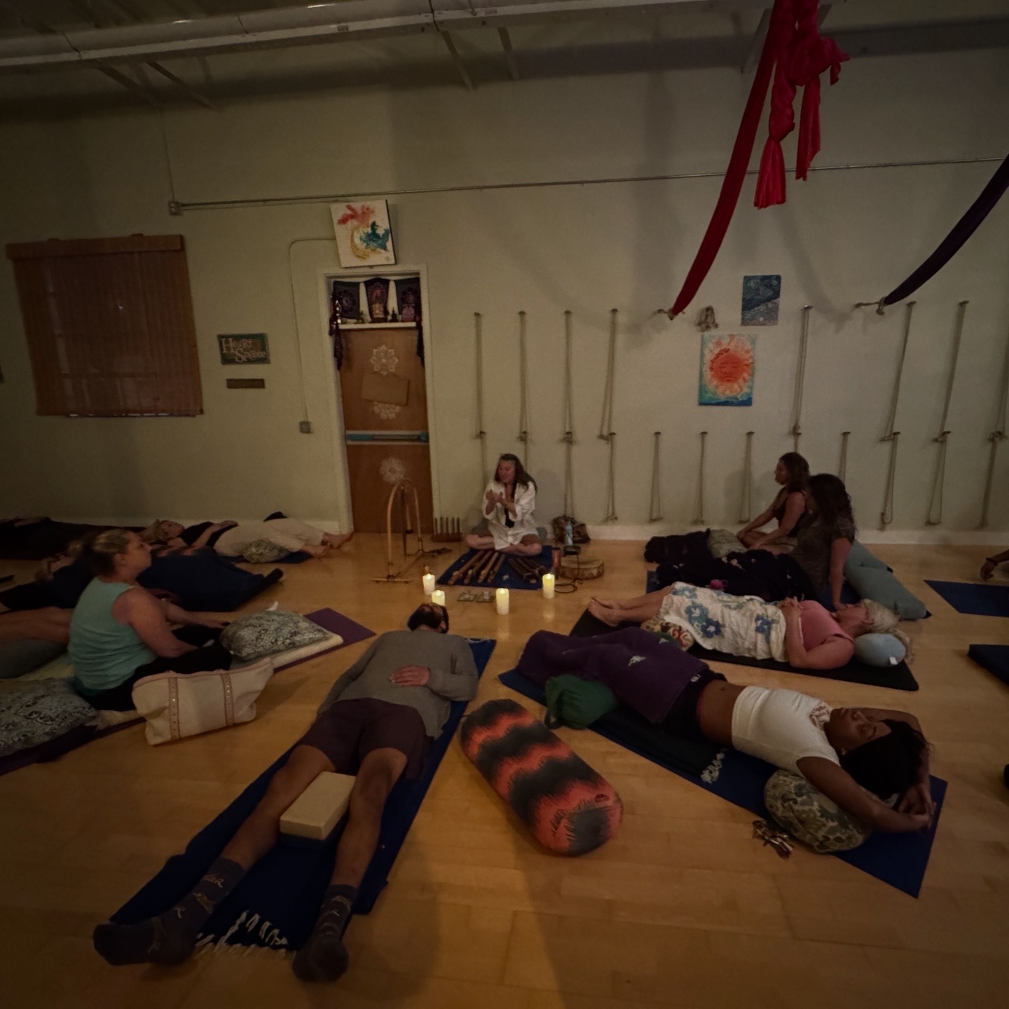 People lying on mats in a room with hanging fabric and wall decorations, participating in a group activity or class.