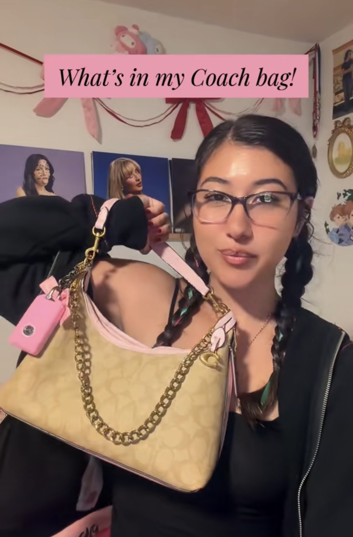 Woman with glasses holding a Coach bag with pink accents and gold chain, in a room with posters and decorations