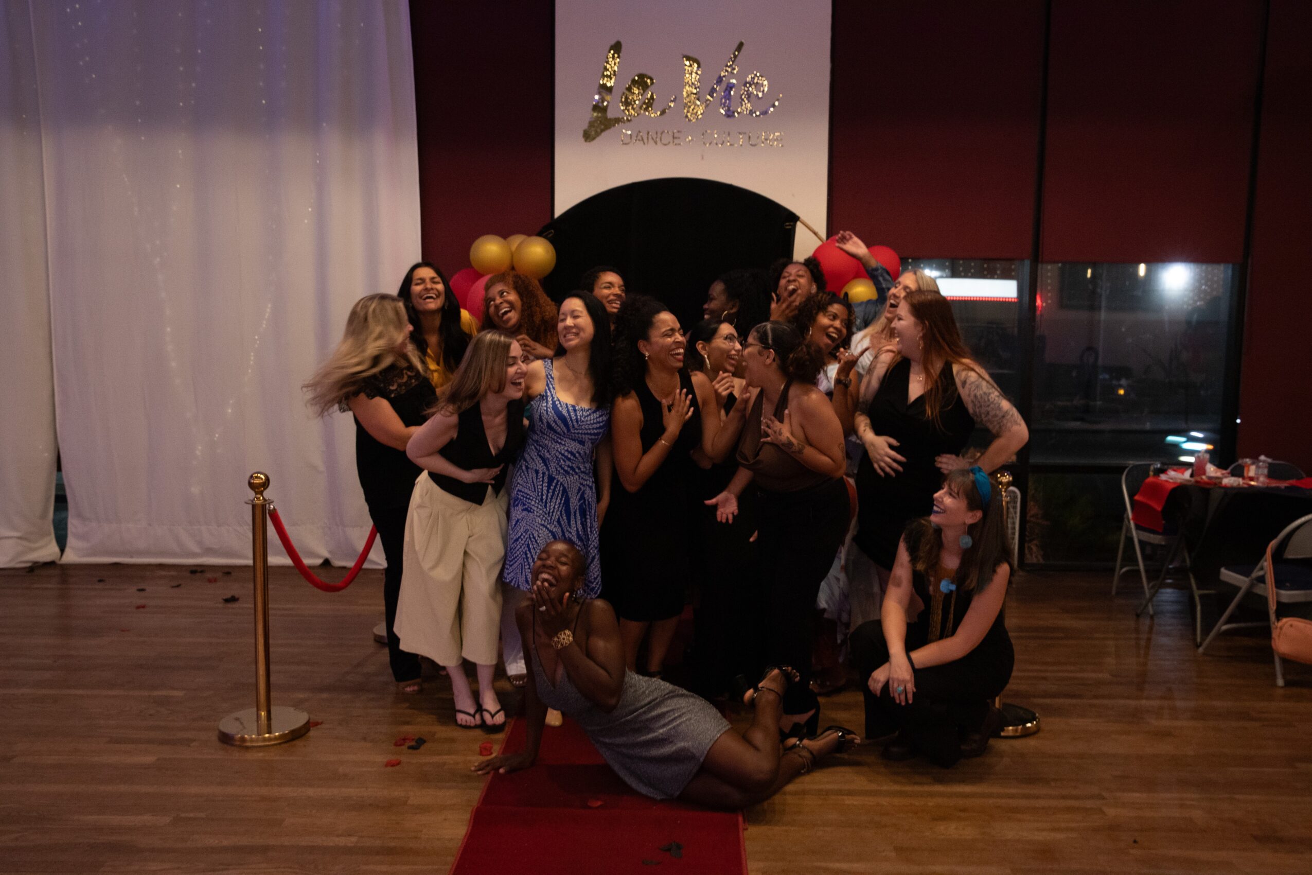 Group of people posing on a stage with a red carpet, balloons, and a