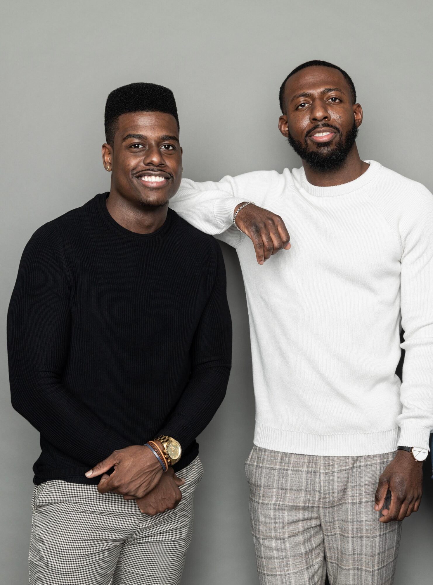Two men standing side by side, smiling, one with arm around the other's shoulder, against a plain background.