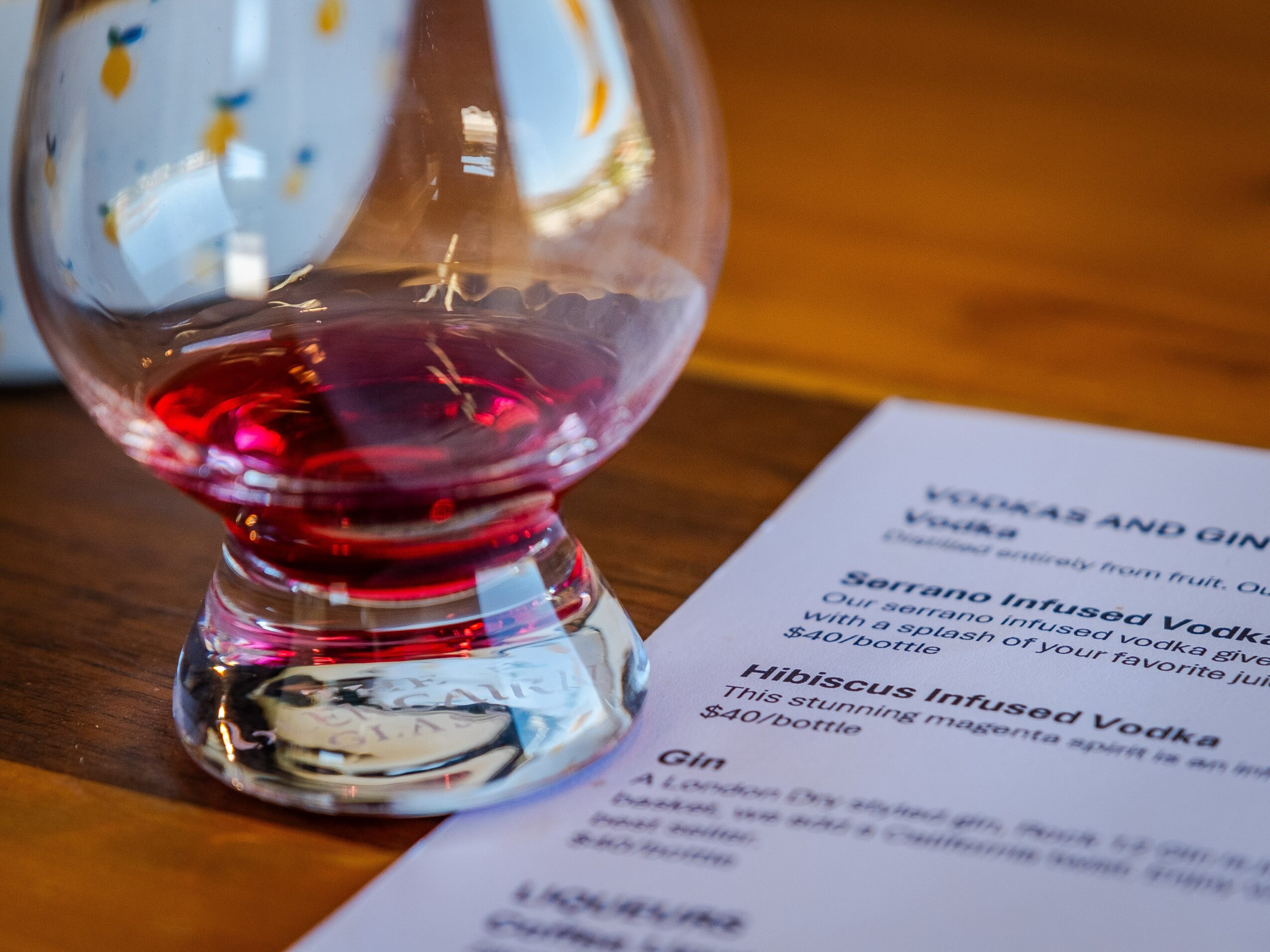 A glass of red wine on a wooden table next to a menu, with reflections on the glass surface.
