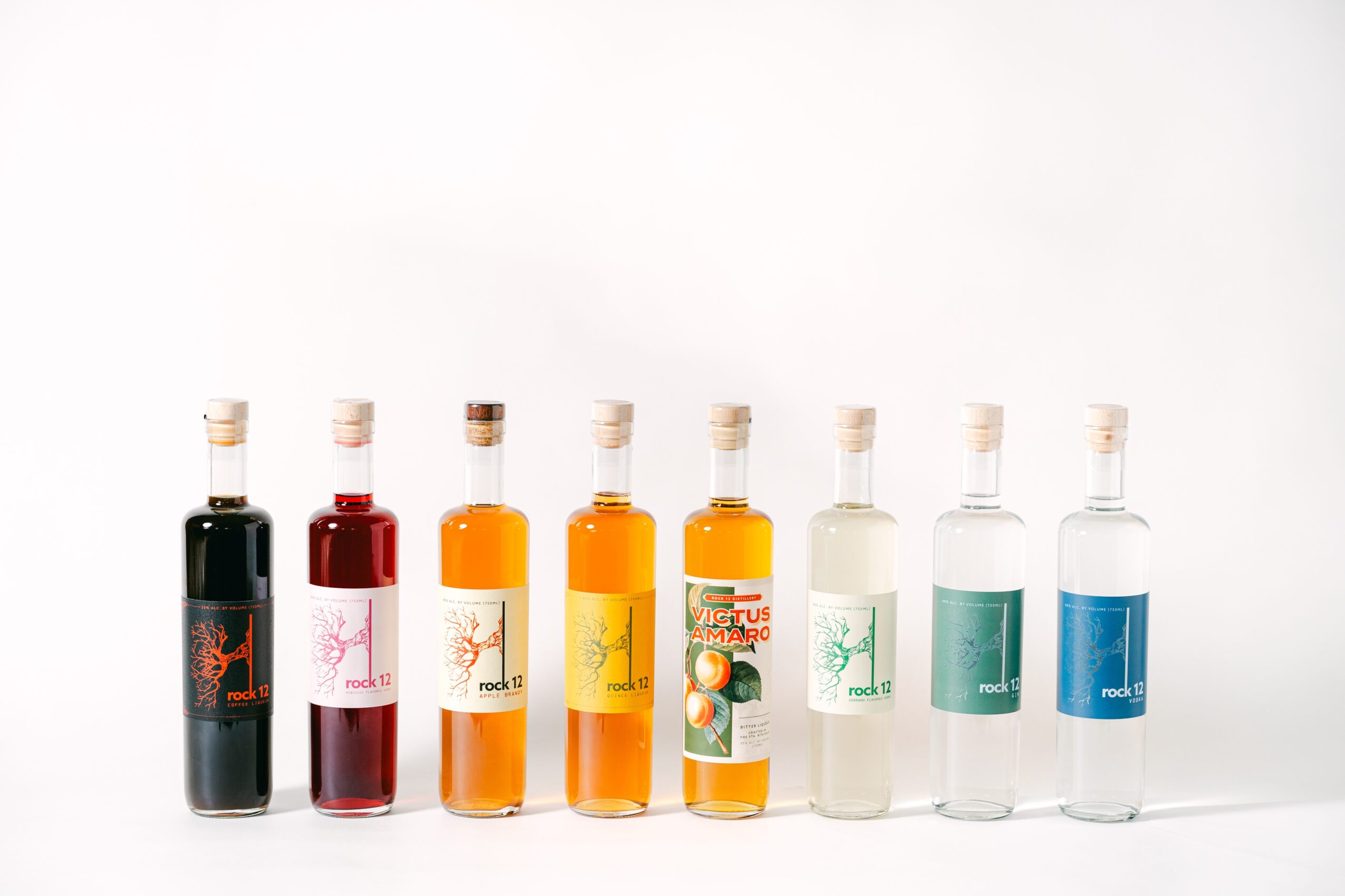 Seven small bottles with colorful liquids arranged in a row on a white background.