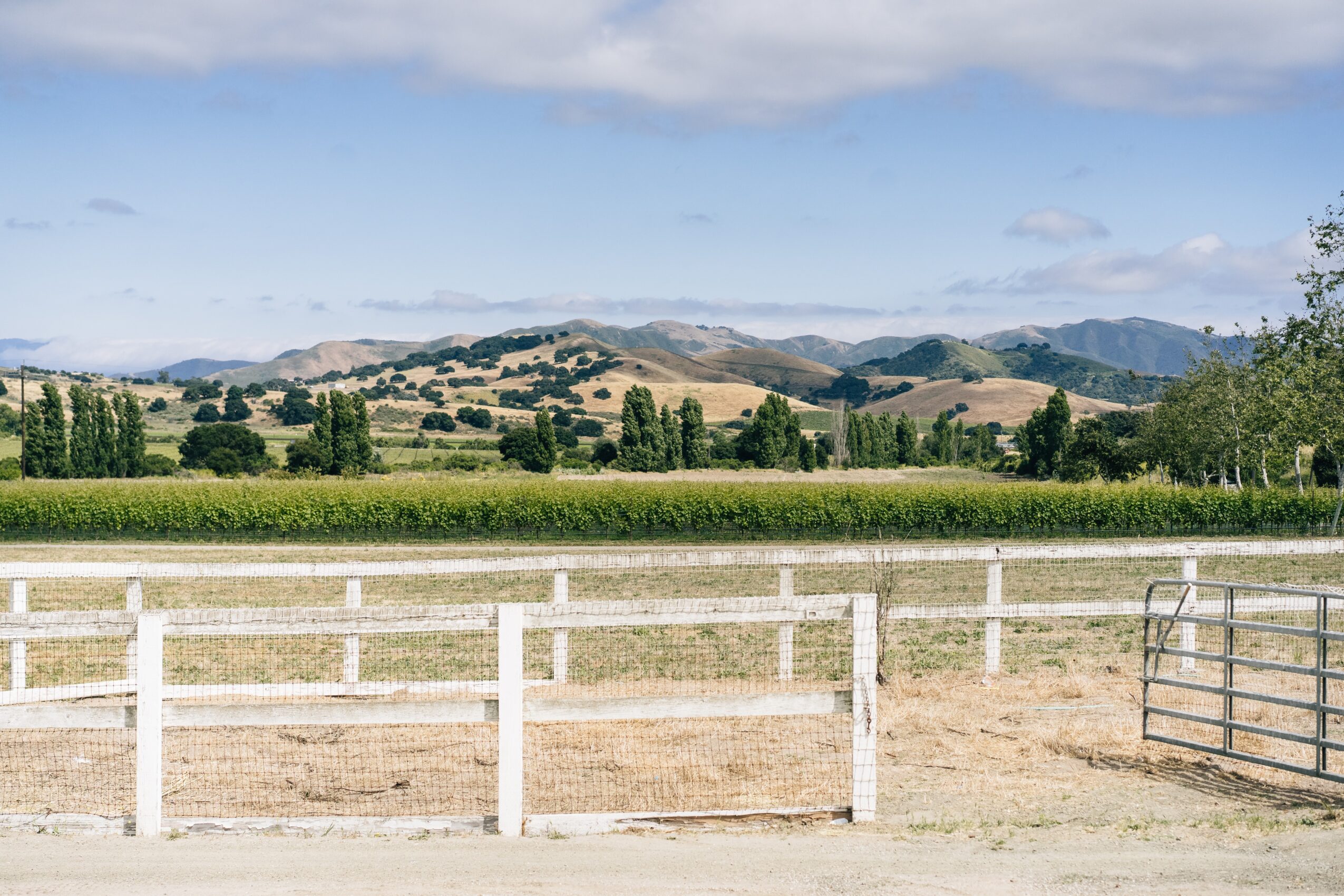 Fenced area with a rural landscape of fields, trees, and hills under a partly cloudy sky.