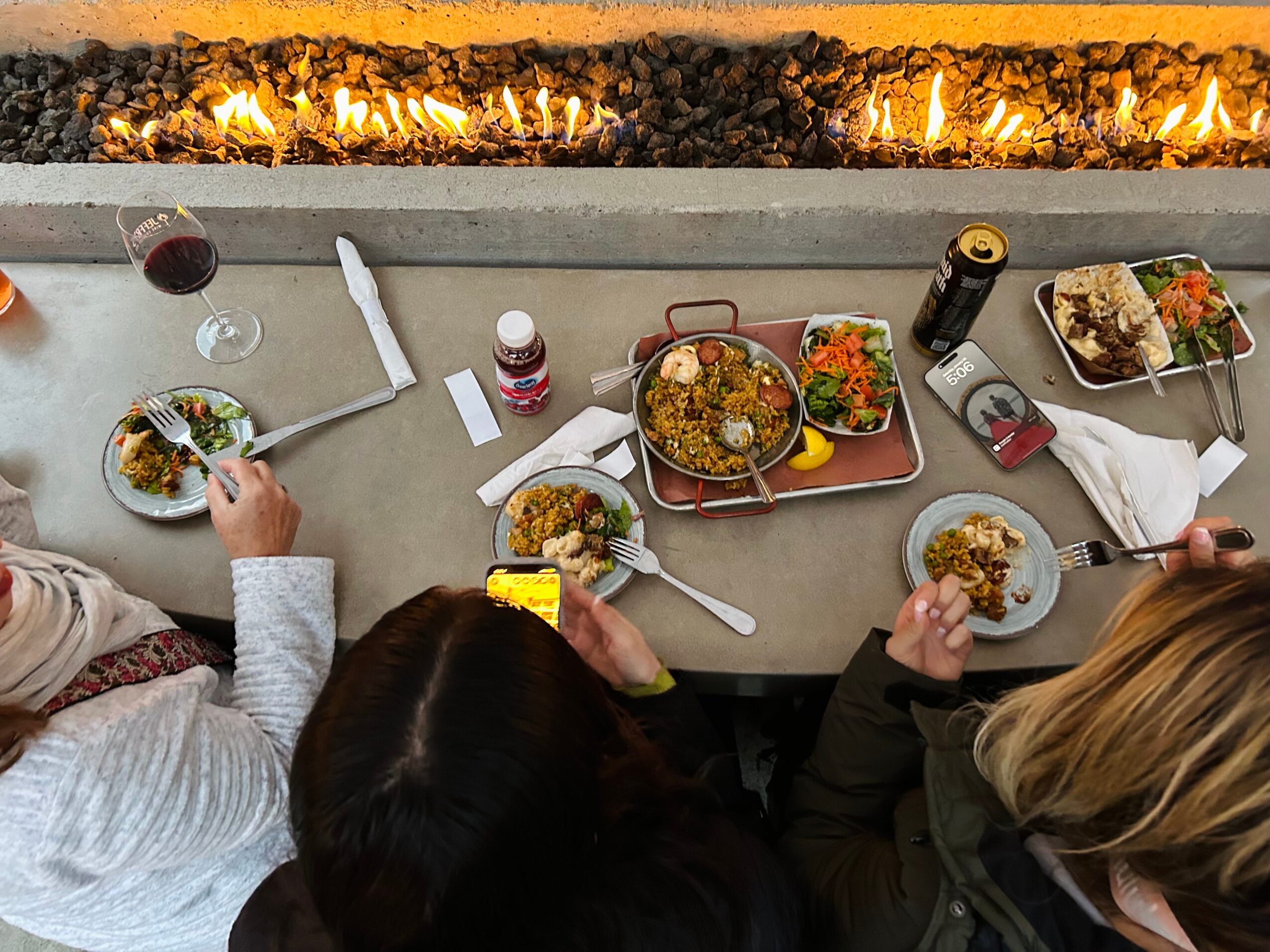 People dining at a table with food, drinks, and condiments, with a fireplace in the background.
