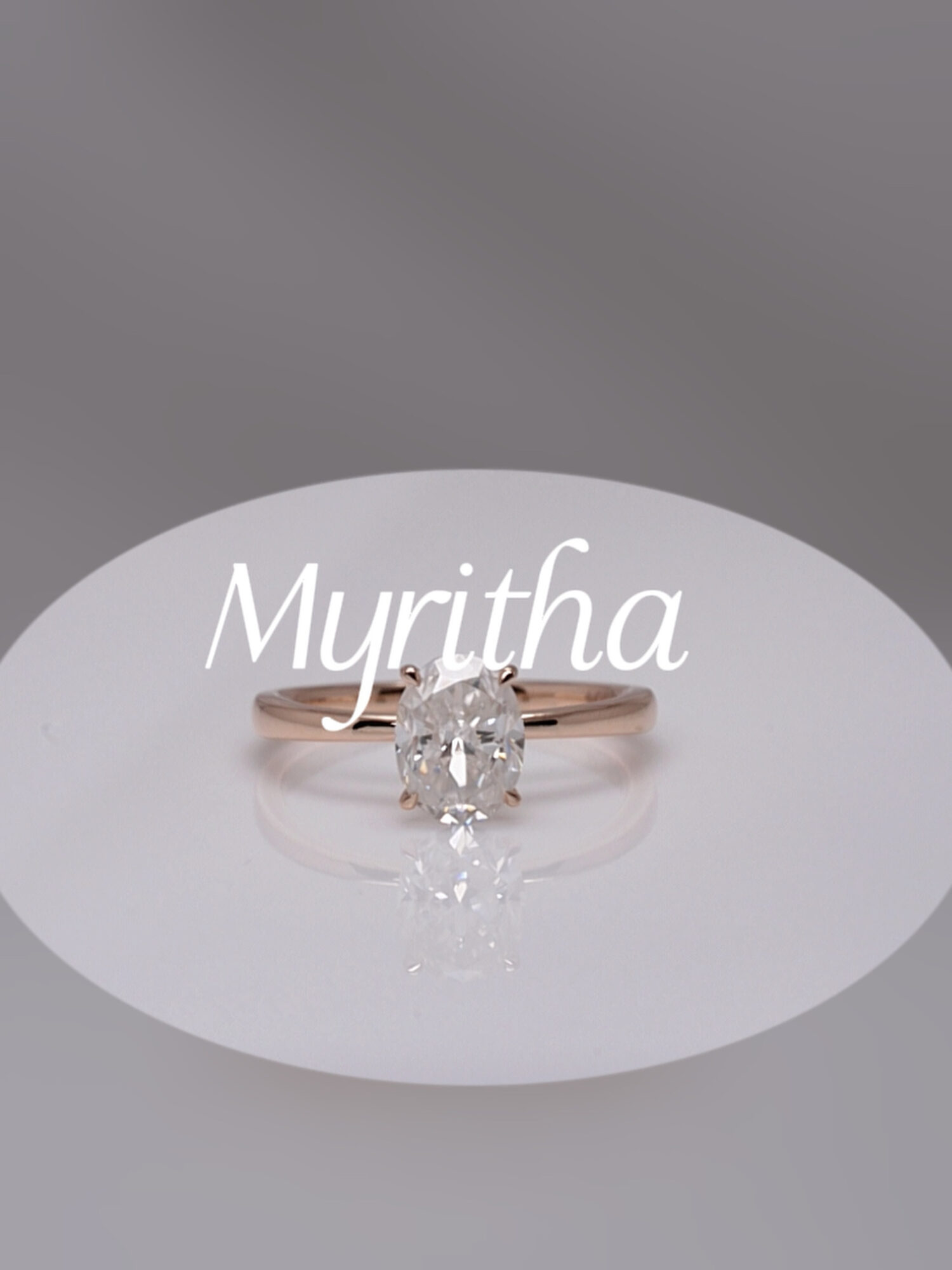 A ring with a large central gemstone on a white surface, with the name 'Myritha' written above, gray background.