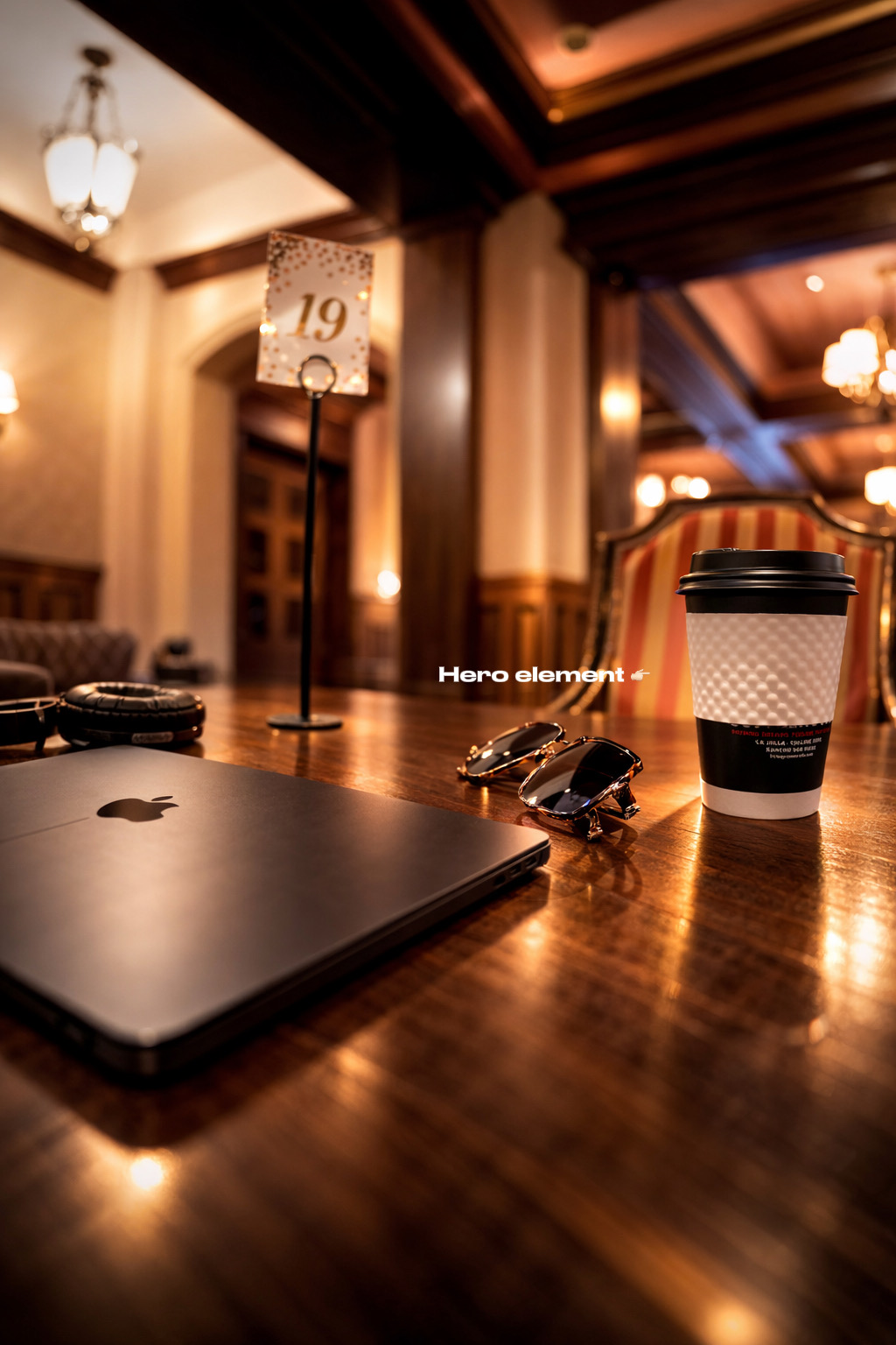 Coffee cup, laptop, and small decorative item on a wooden table in a warmly lit room.