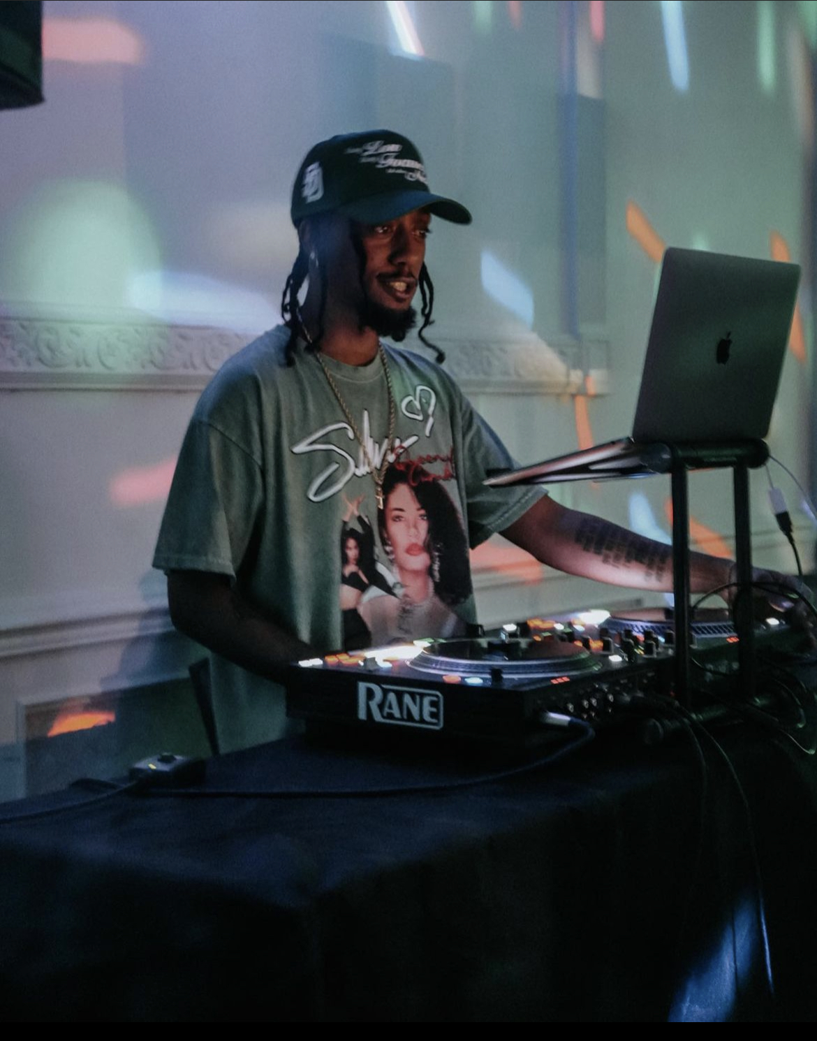 DJ with headphones and a cap, using a laptop and DJ equipment at a party or event.