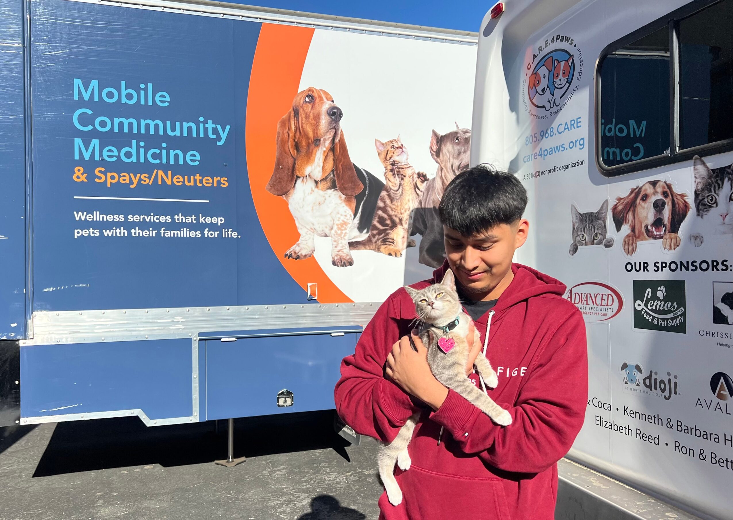 Young boy holding a small dog in front of a mobile community medicine truck with images of dogs and sponsors.