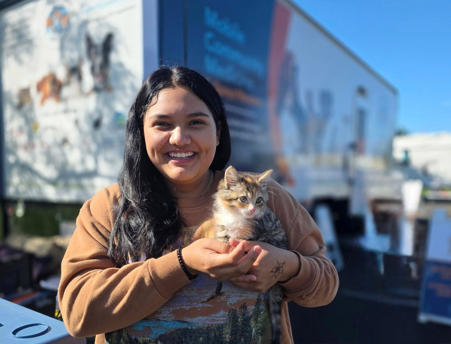 Woman holding a cat outdoors with a large building and blue sky in background.