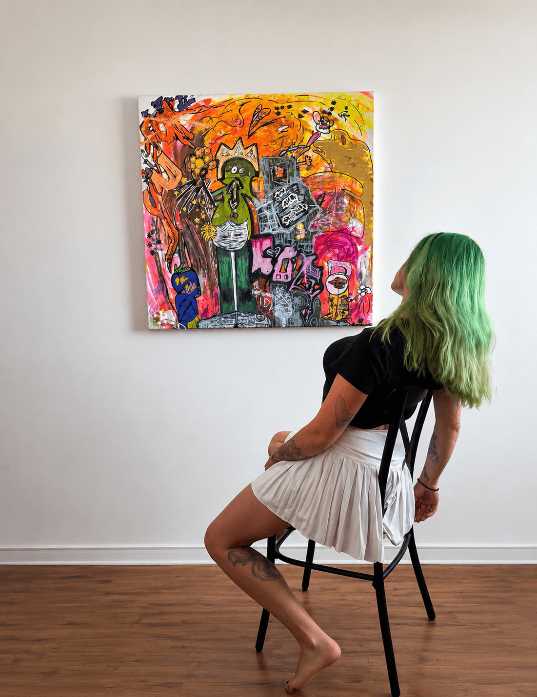 Person with green hair sitting on a chair, looking at colorful abstract painting on white wall, wooden floor.