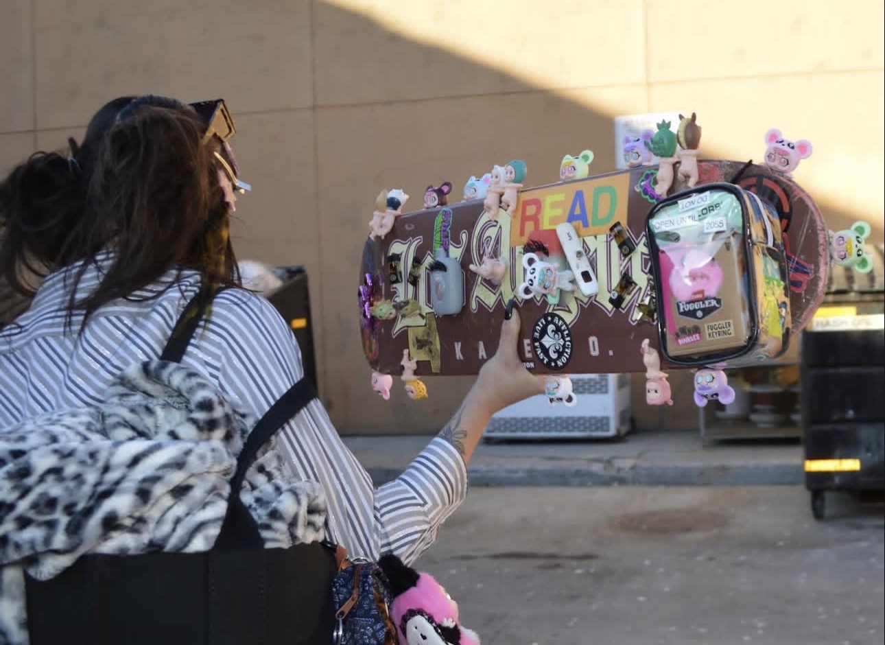 Person with striped shirt and backpack reaching for decorated suitcase with stickers and toys, parked outdoors.