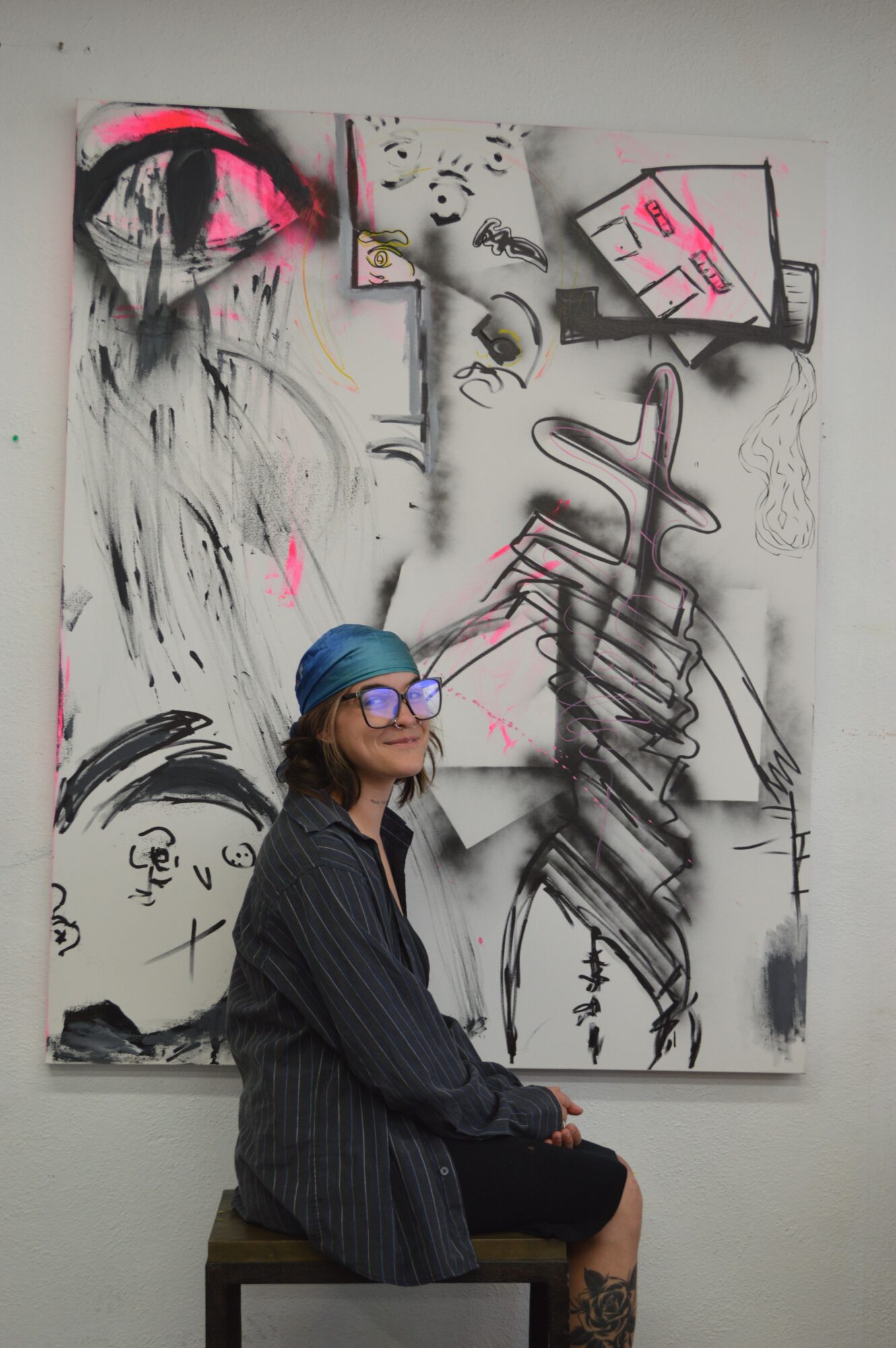 Person with blue cap and glasses looking at abstract black, white, and pink artwork on wall.