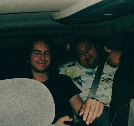 Two people sitting in a car, one smiling and the other giving a thumbs-up, both wearing seatbelts.