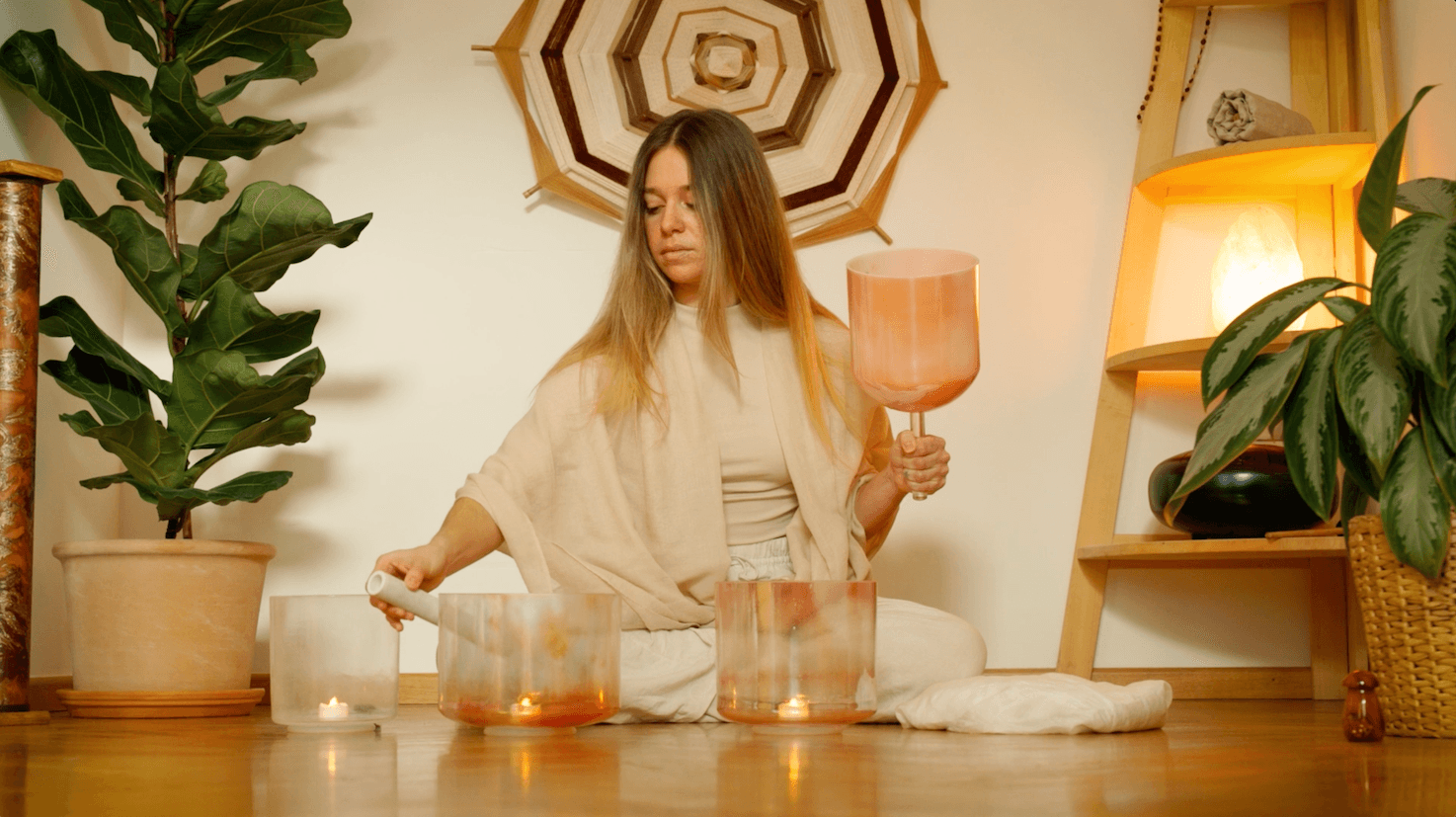 Woman with long hair holding a large glass, surrounded by plants and warm lighting, sitting at a table with candles.