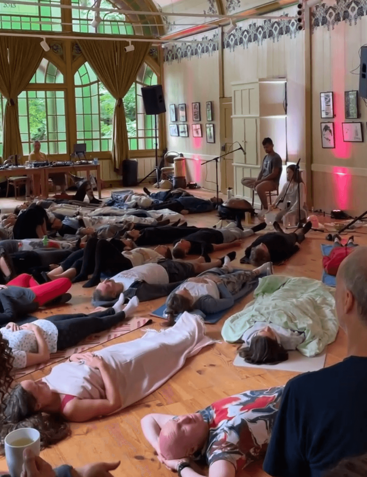 People lying on the floor in a large room with tall windows, curtains, and framed pictures on the walls.