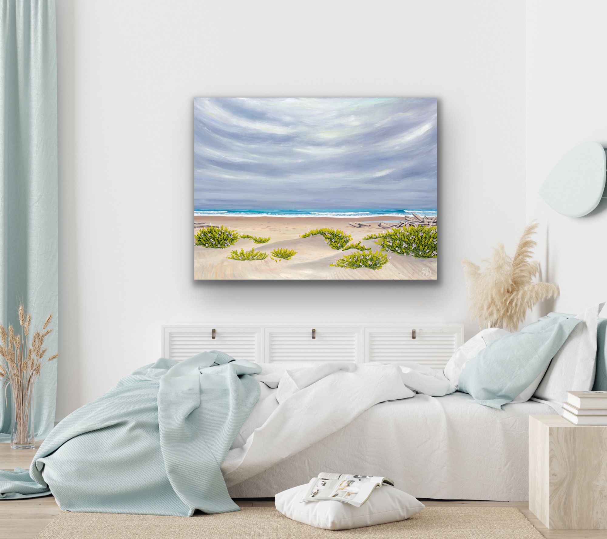 Beach scene with sand, green plants, and cloudy sky, hanging above a bed in a bright bedroom.
