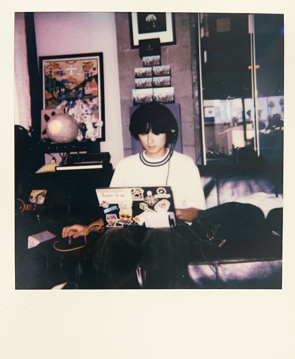 Person with black hair reading a magazine in a room with purple walls, framed pictures, and a glass door.