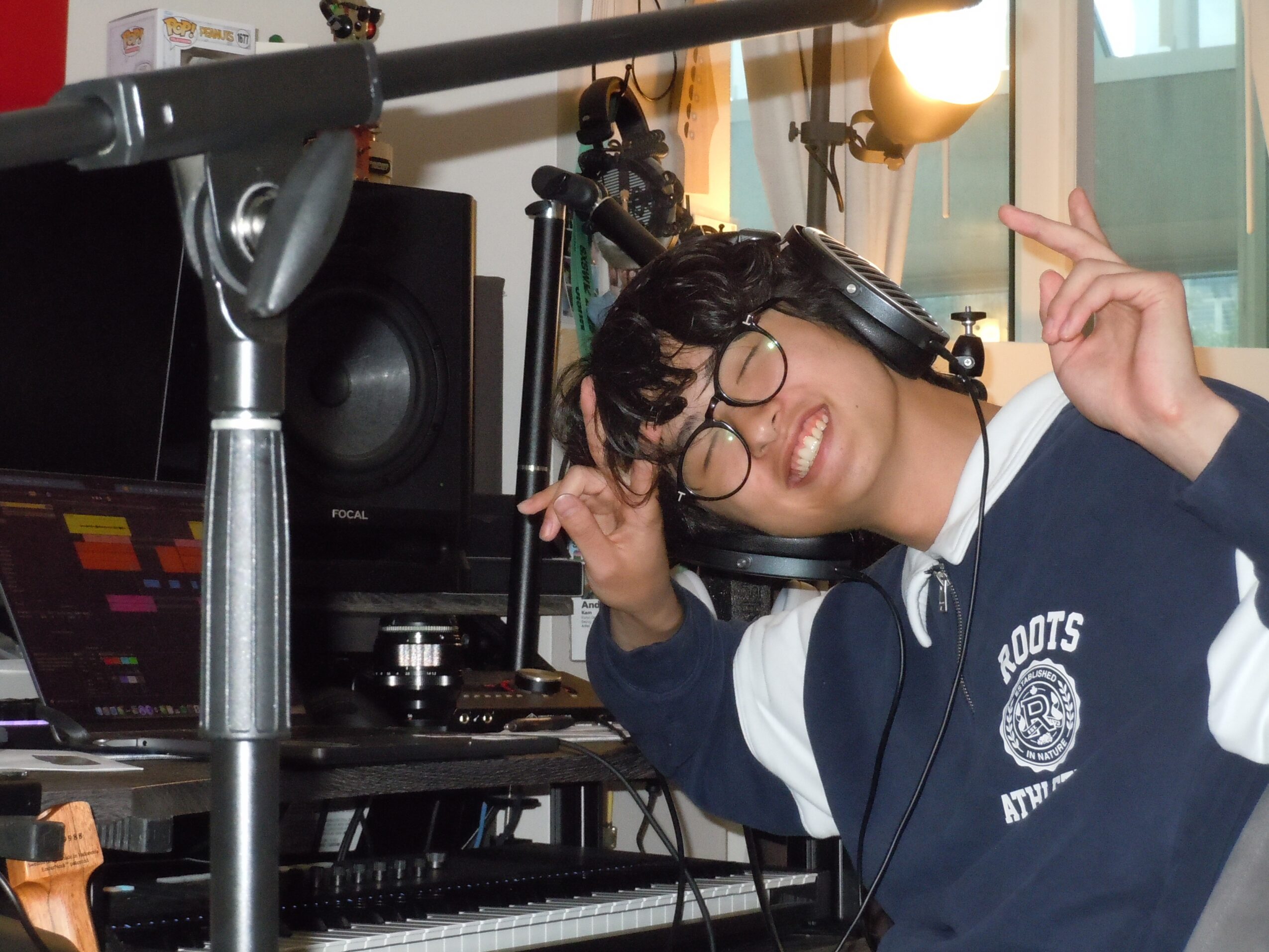 Person with glasses smiling, wearing headphones, making a peace sign in a recording studio.