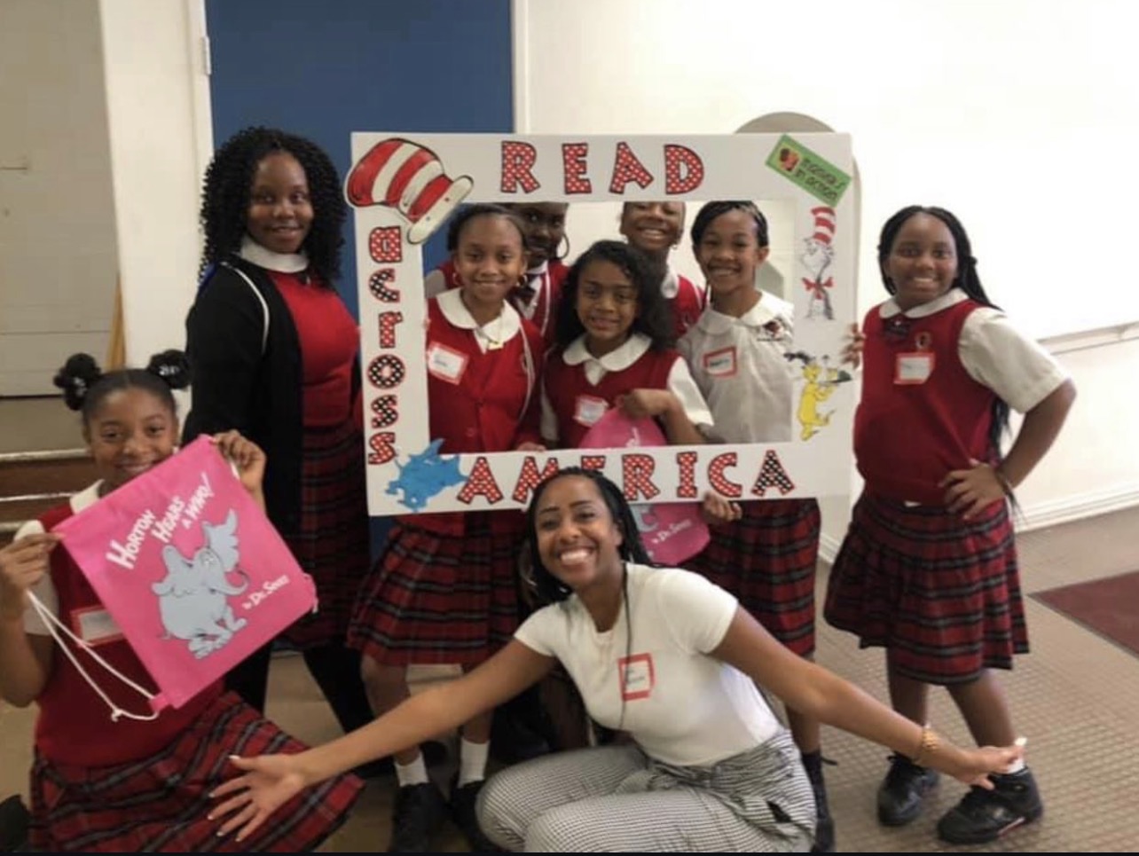 Group of children and an adult posing with a large frame reading 'READ' and 'AMERICA' in a classroom.