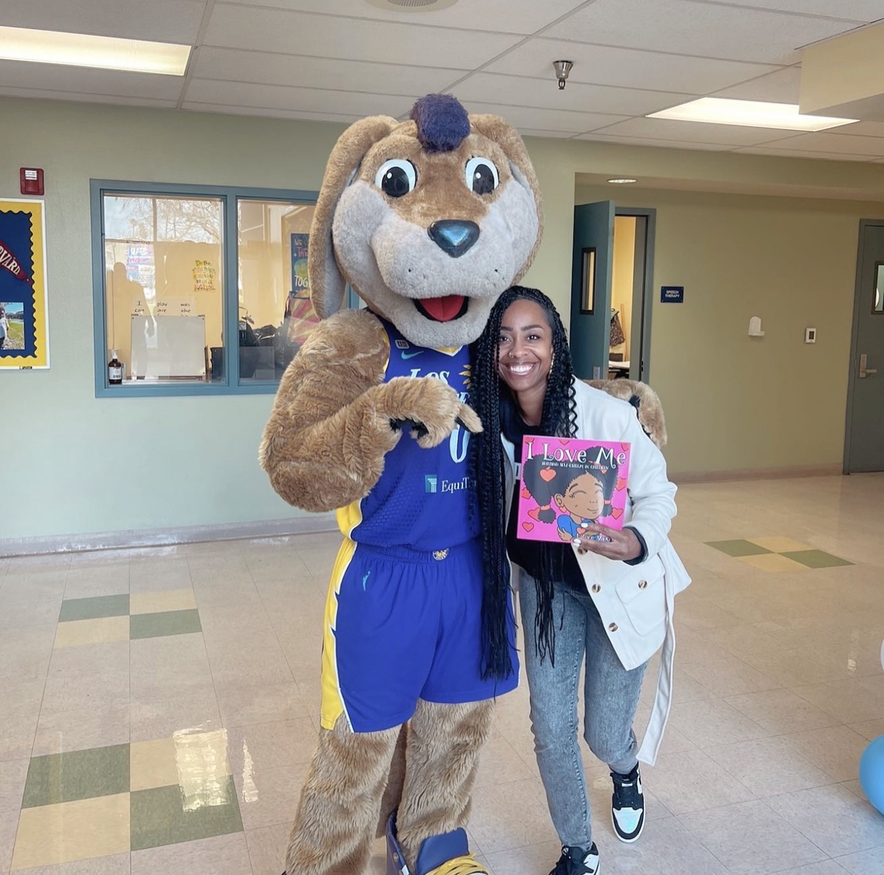 Person in a bunny mascot costume standing next to a smiling woman holding a colorful drawing, indoors.