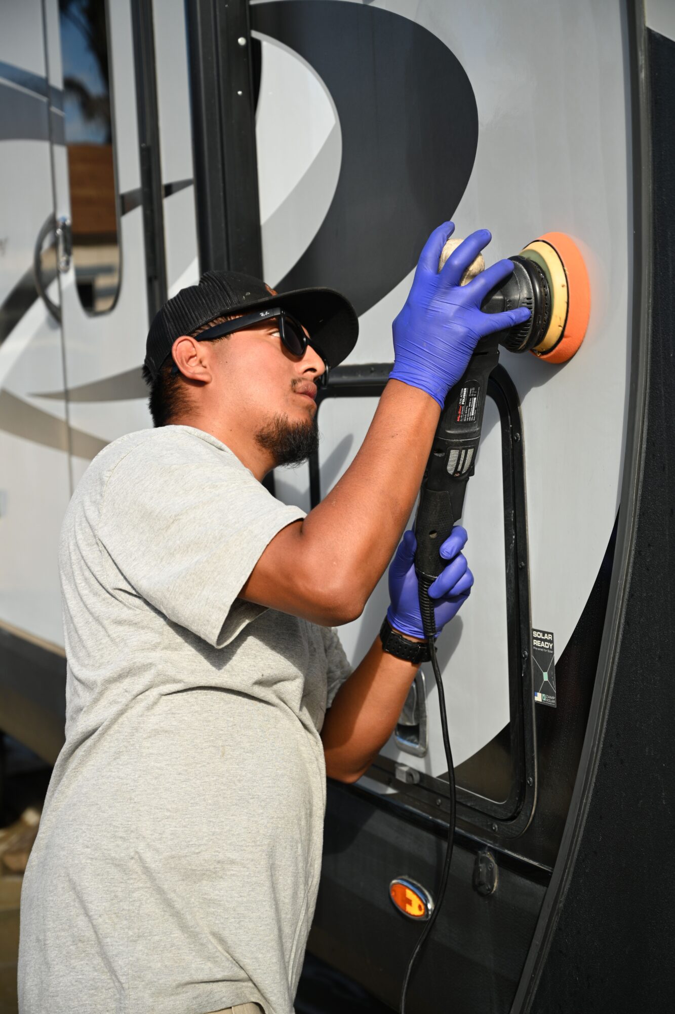Person wearing a gray shirt and blue gloves polishes a car's hood with a circular buffer tool.