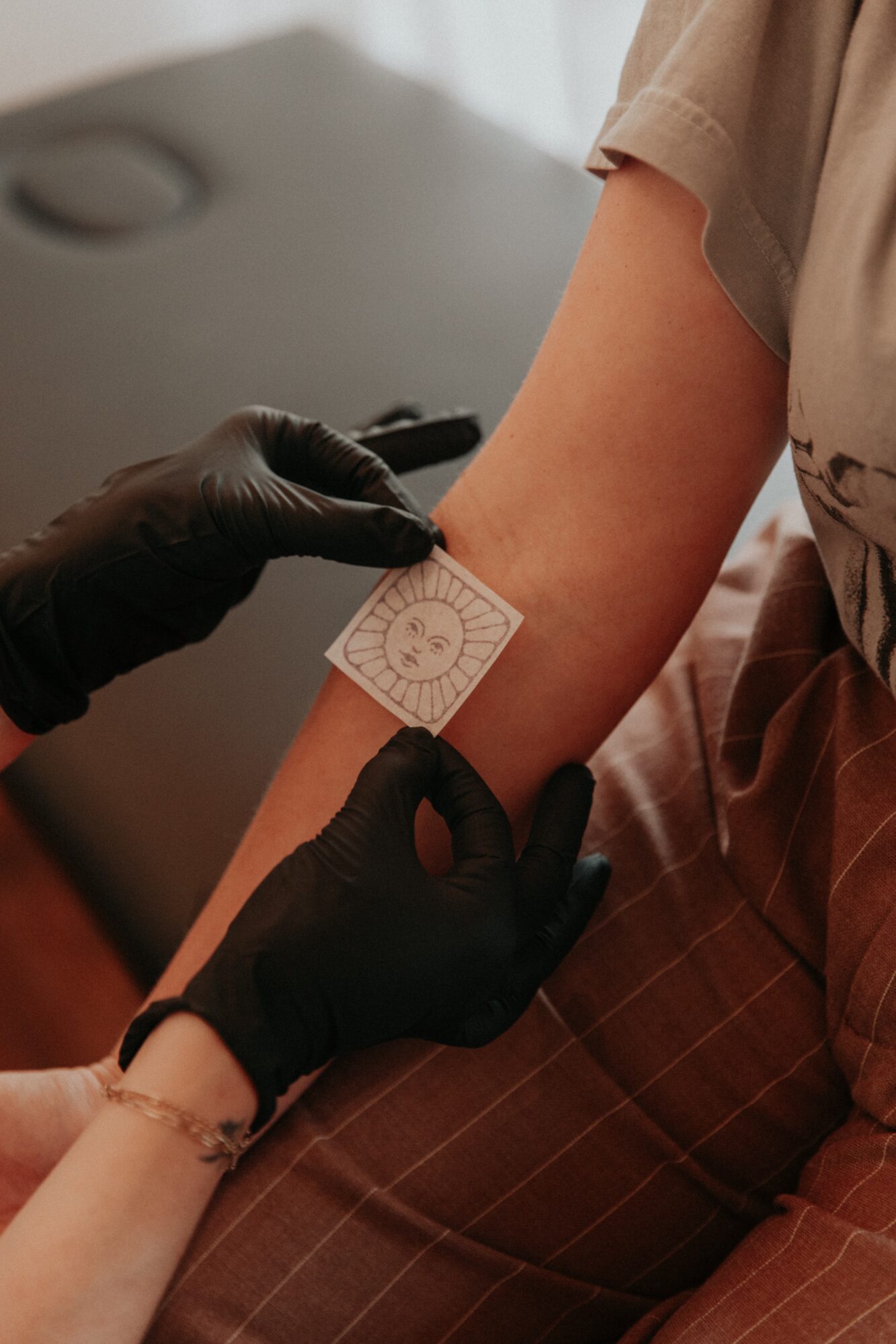 Person's arm with a bandage being applied by a healthcare worker wearing black gloves.