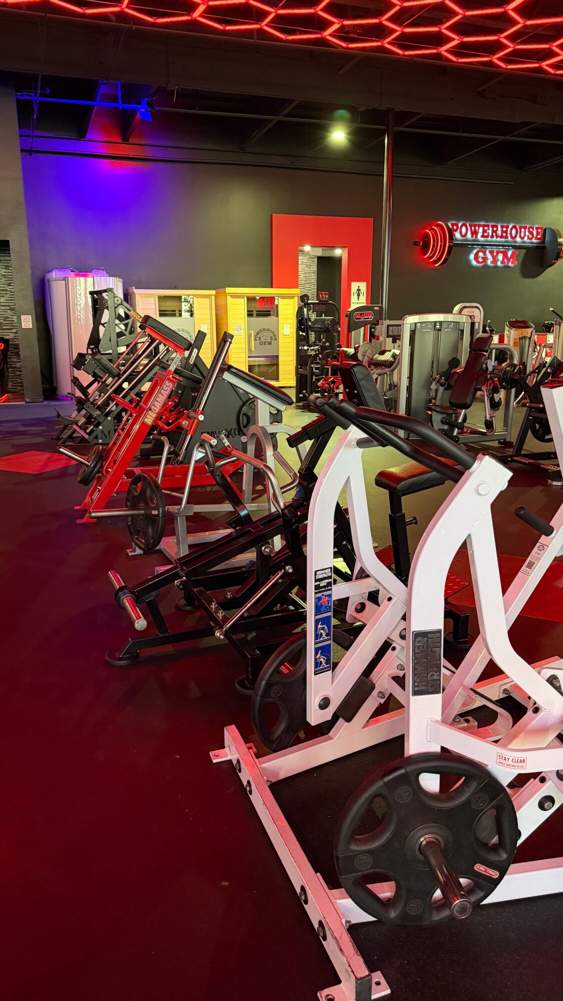 Gym with exercise bikes, weight machines, and colorful lighting, including red, purple, and green lights, in a fitness center.