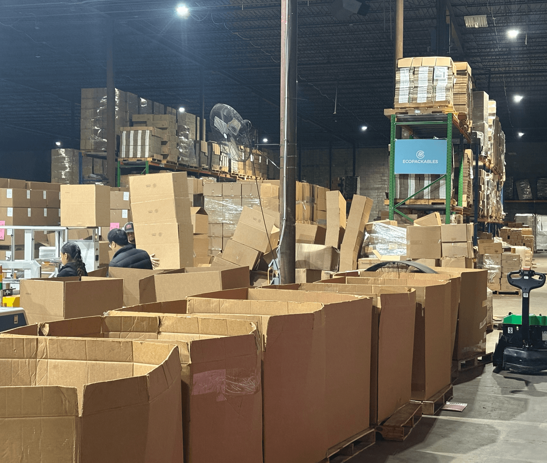 Warehouse with stacked boxes and workers, some boxes are open, and a forklift is visible in the background.