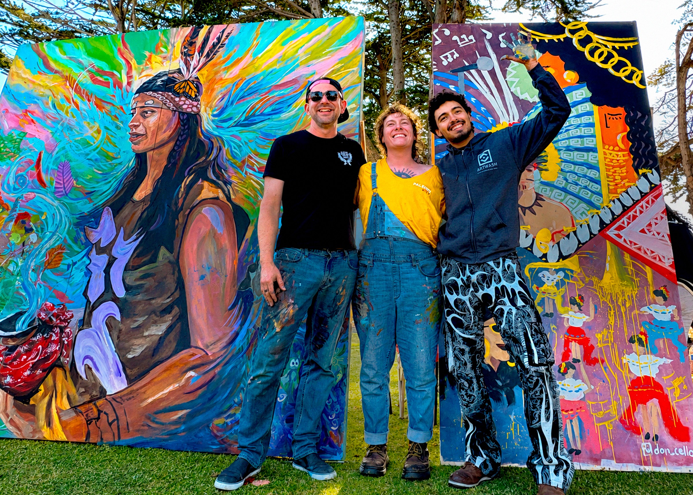 Three people stand outdoors in front of colorful murals, smiling and posing for the photo.