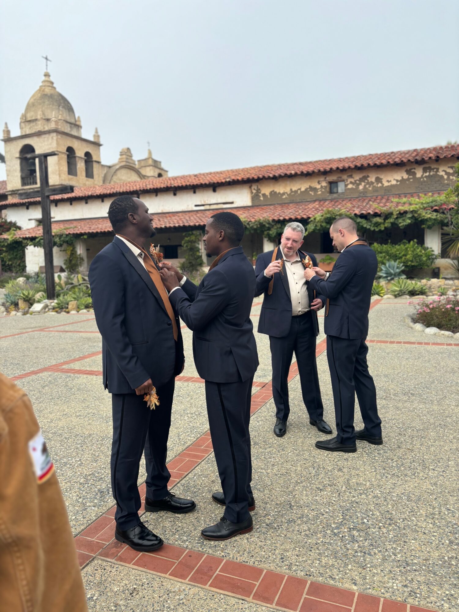 Four men in suits are talking outdoors near a building with a bell tower, with a church in the background.