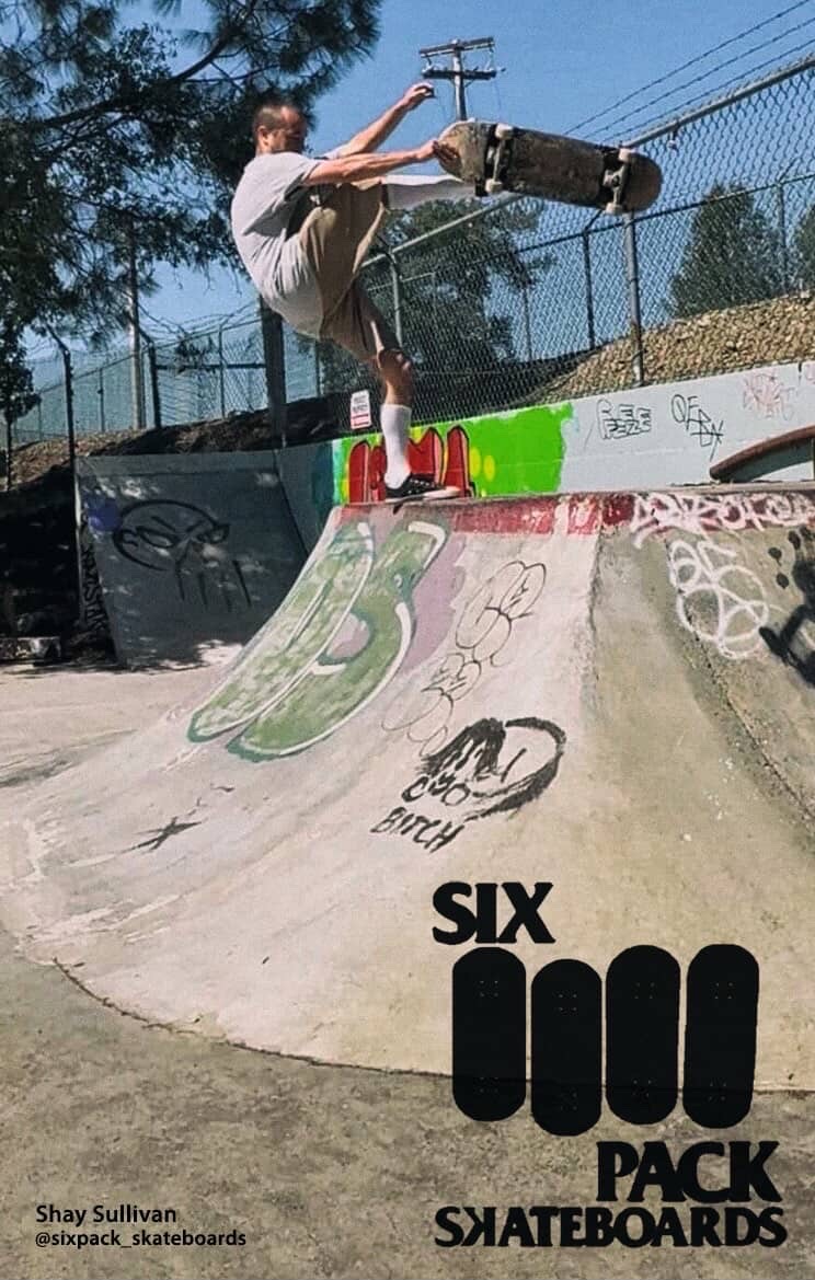 Skateboarder in mid-air at skatepark with graffiti, fence, and trees in background, performing a trick on a ramp.