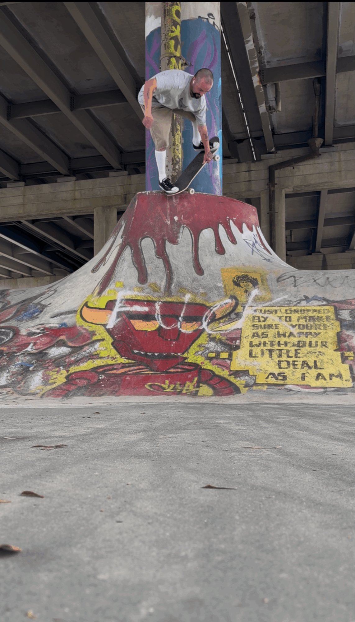 Child climbing on a colorful skate park ramp with a yellow sign, concrete ground, and a roof structure overhead.