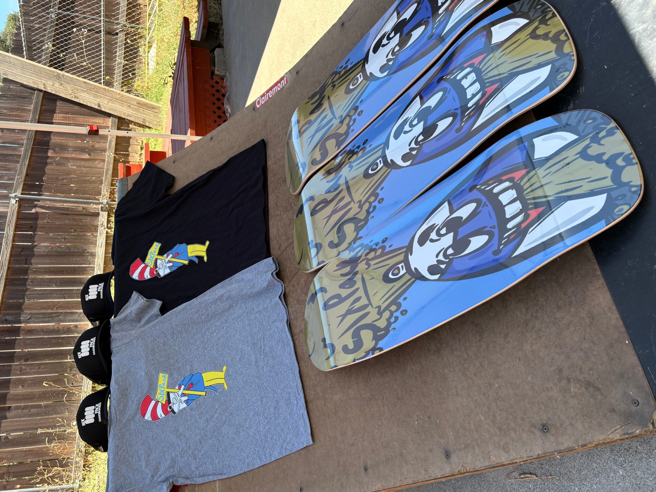 Skateboards with cartoon character designs, T-shirts, and shoes on a table outdoors.