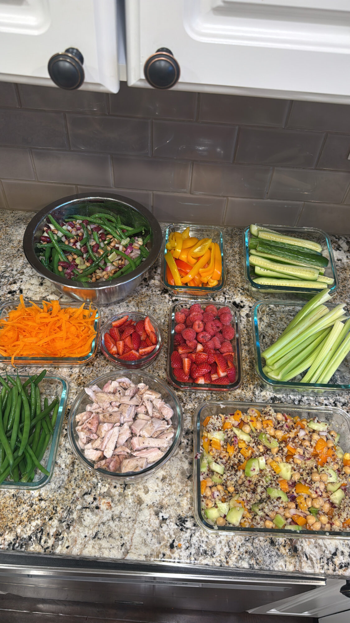 Assorted fresh vegetables and salad ingredients on a kitchen countertop, including greens, bell peppers, celery, carrots, tomatoes, and a prepared salad.