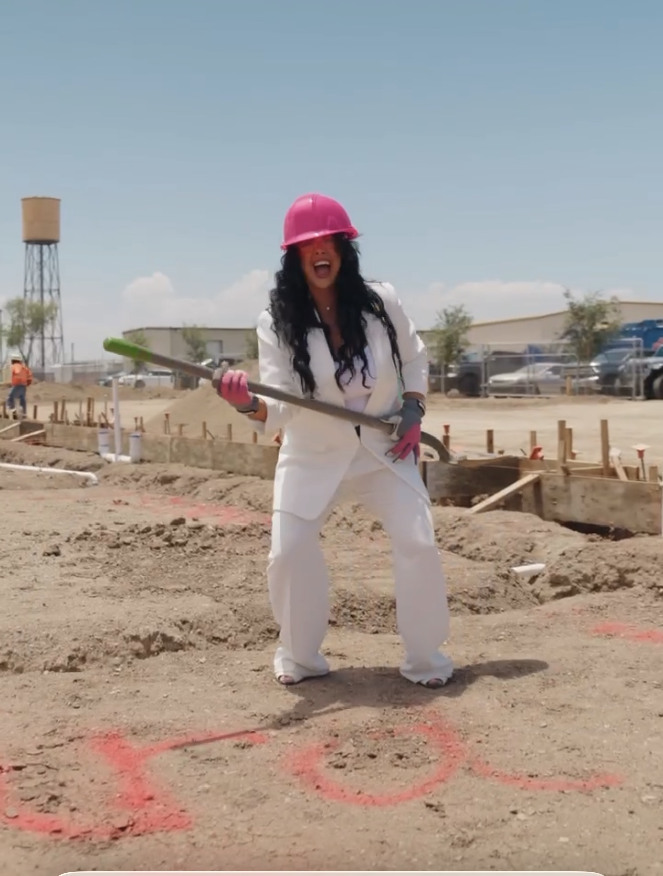 Person wearing a pink helmet and white outfit holding a shovel on a construction site.